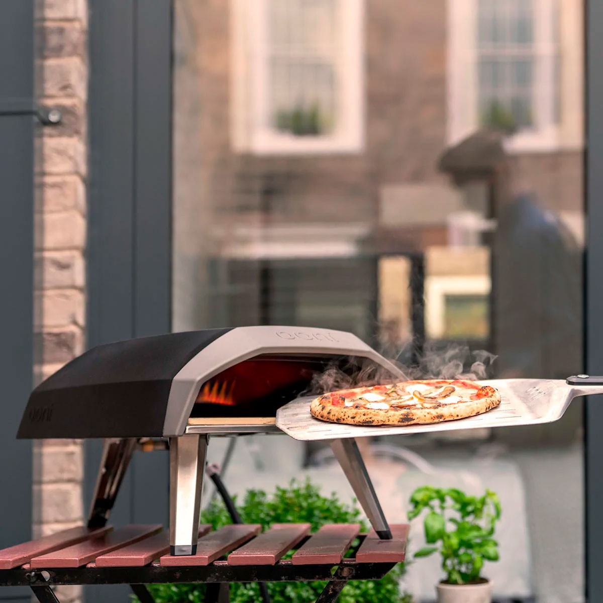 Una pizza viene rimossa da un forno per pizza all'aperto su un tavolo, di fronte a una porta a vetri.