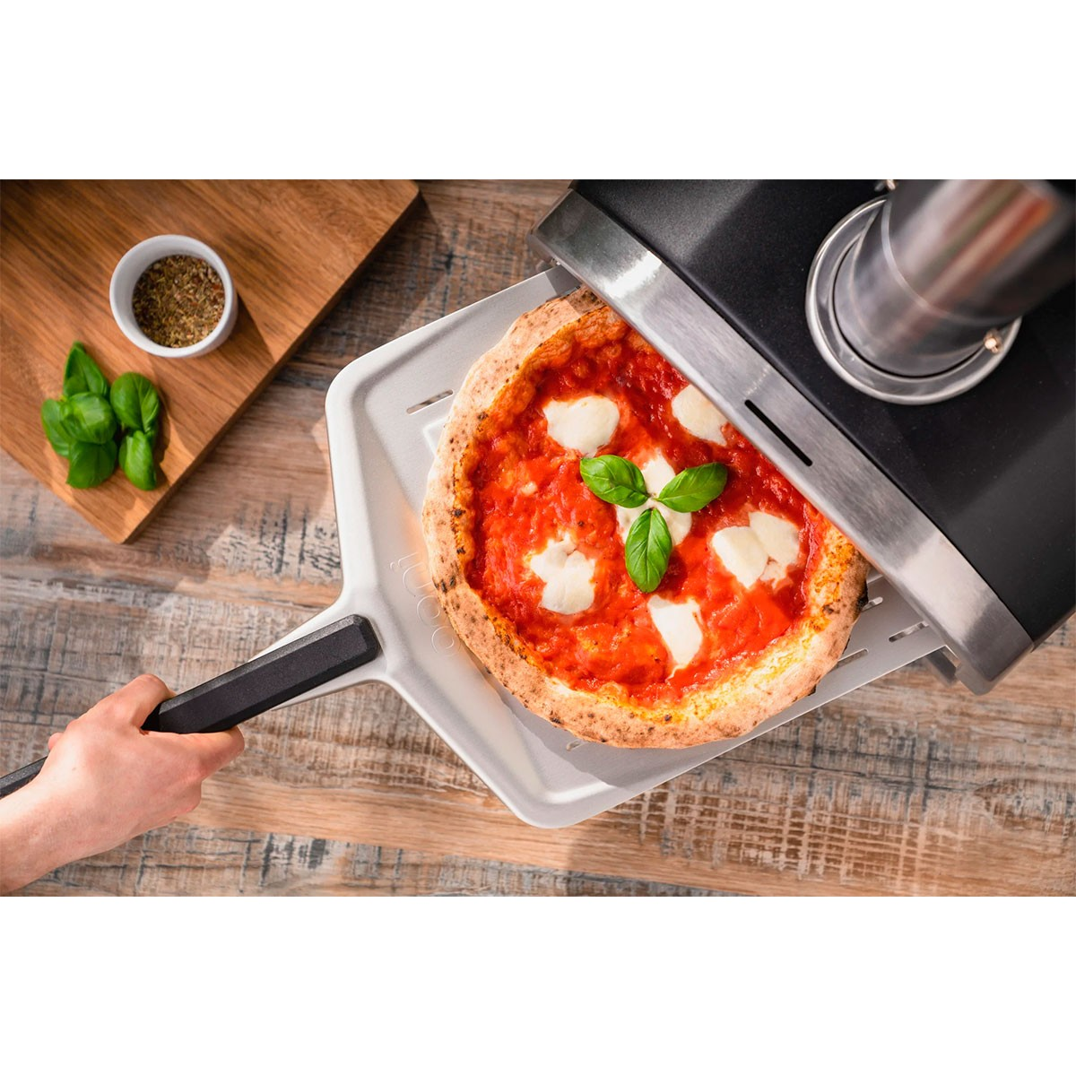 Pizza rimossa dal forno su una pala. Guarnizione di basilico sopra.