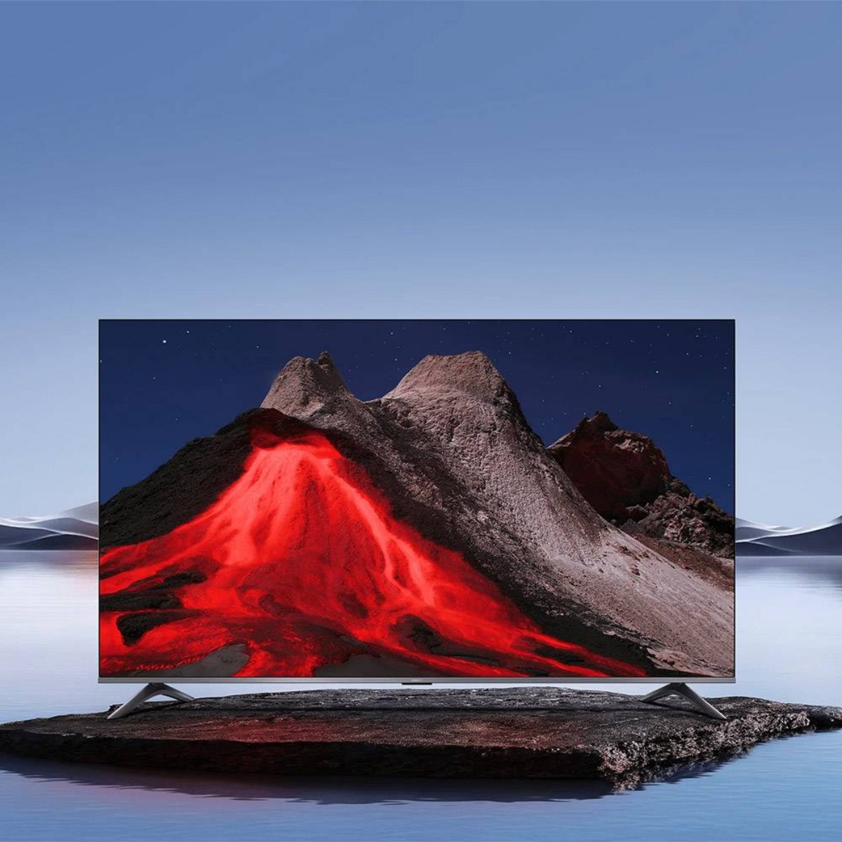 Duży telewizor pokazujący czerwony strumień lawy, nocne niebo i pasmo górskie. Telewizor stoi na skale.