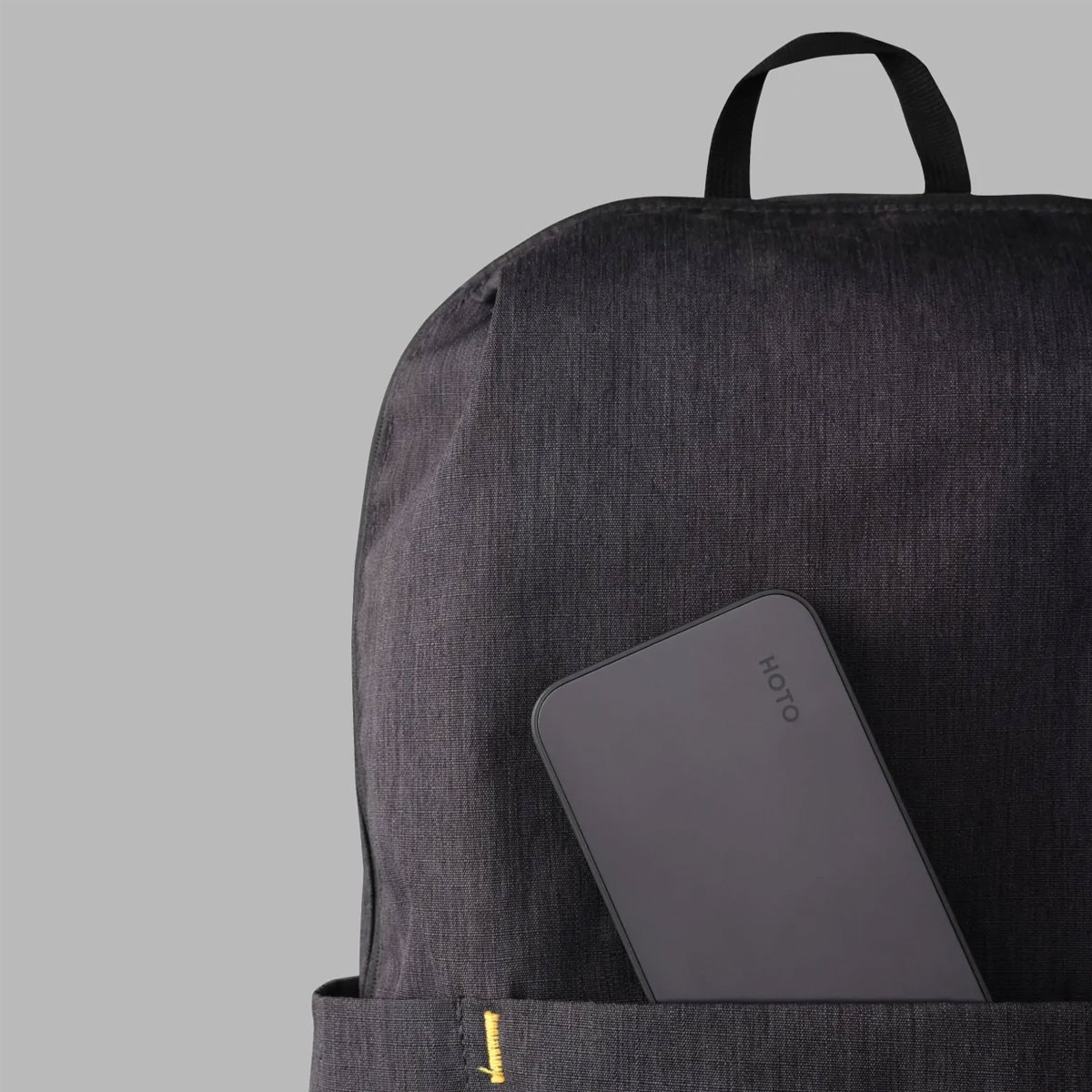 Ein schwarzer Rucksack mit einer grauen Geldbörse in der Vordertasche. Grauer Hintergrund.
