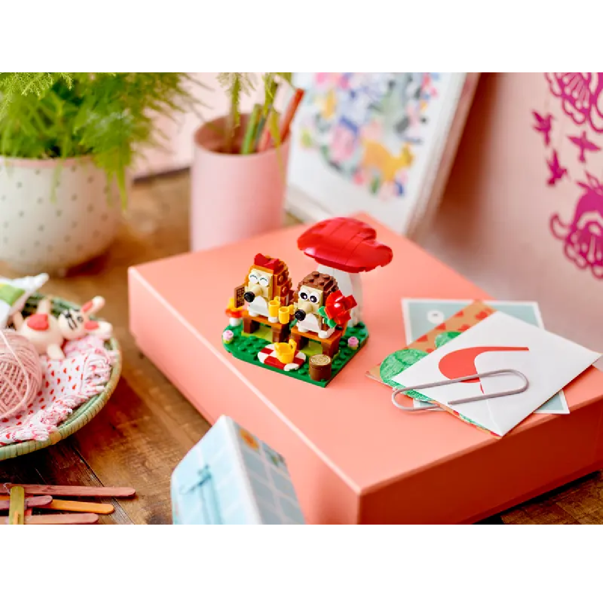 Zestaw LEGO: Dwie figurki jeży siedzą na ławce z grzybem, na różowym pudełku.