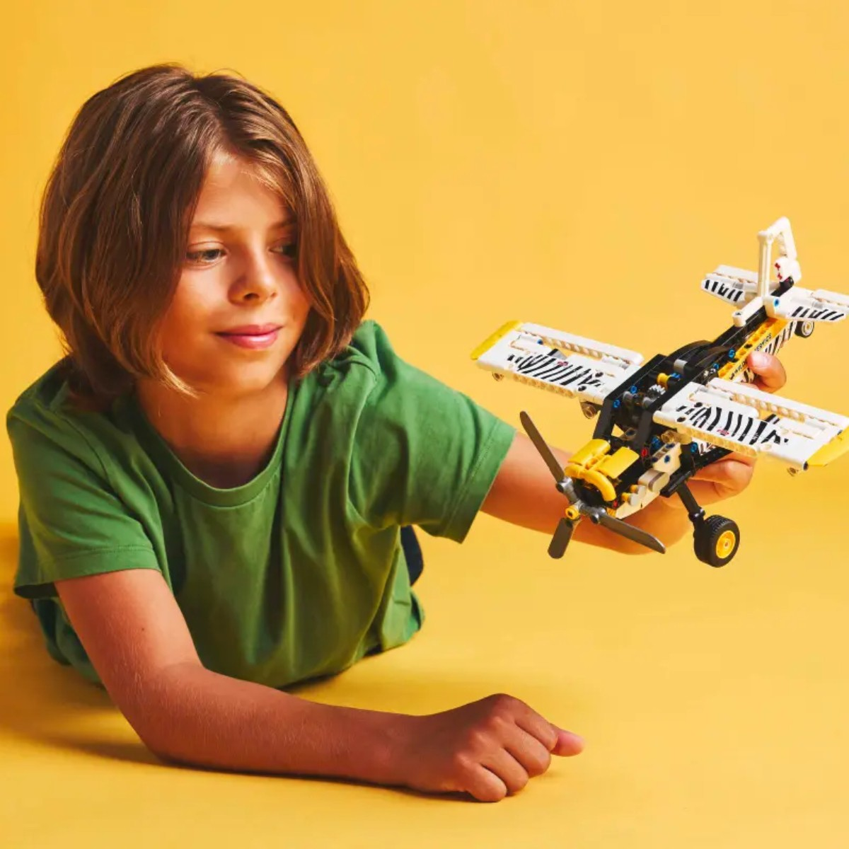 Dziecko trzymające żółto-biały model LEGO dwupłatowca na żółtym tle.