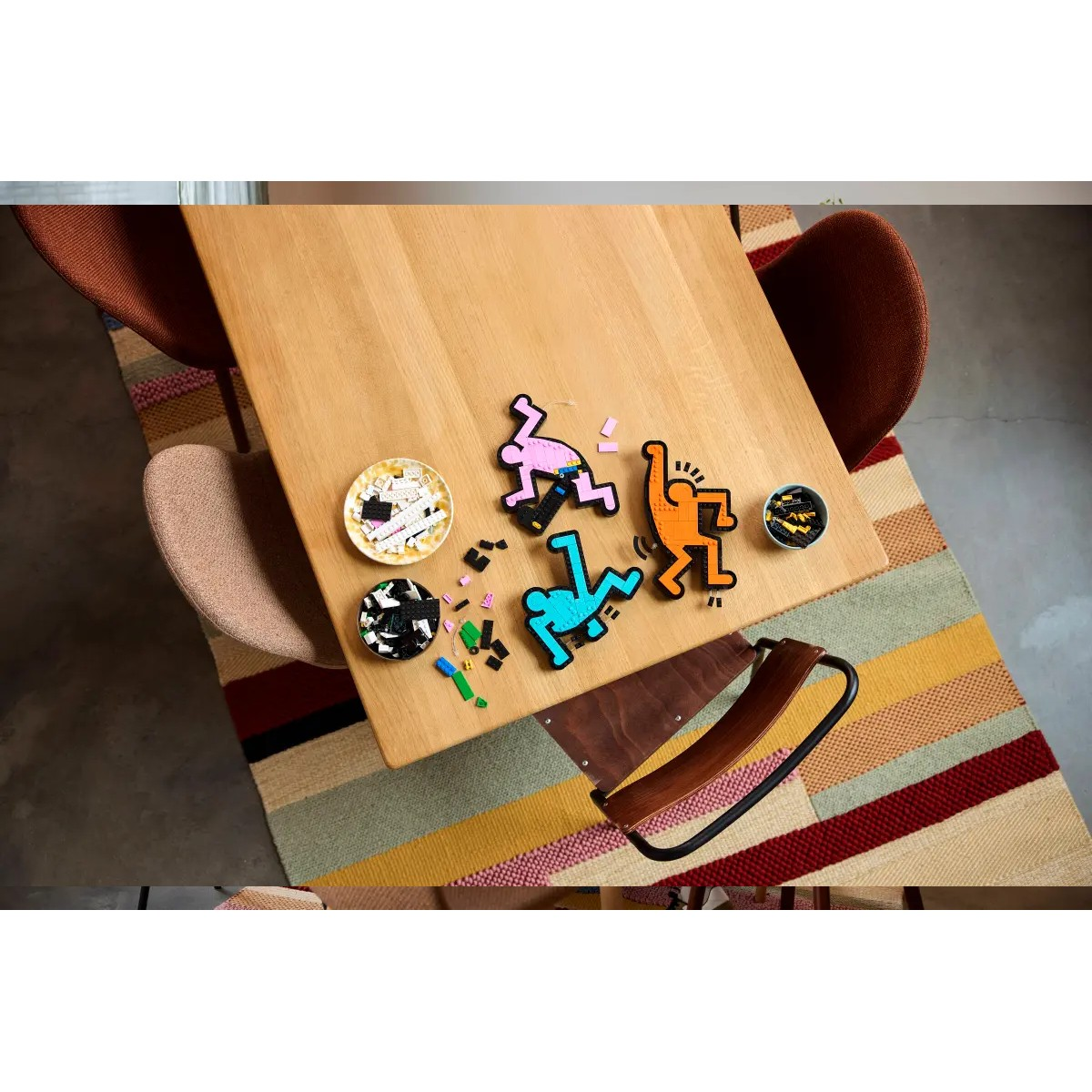 Drewniany stół z kolorowymi figurkami Keitha Haringa i dywanem z wzorem.