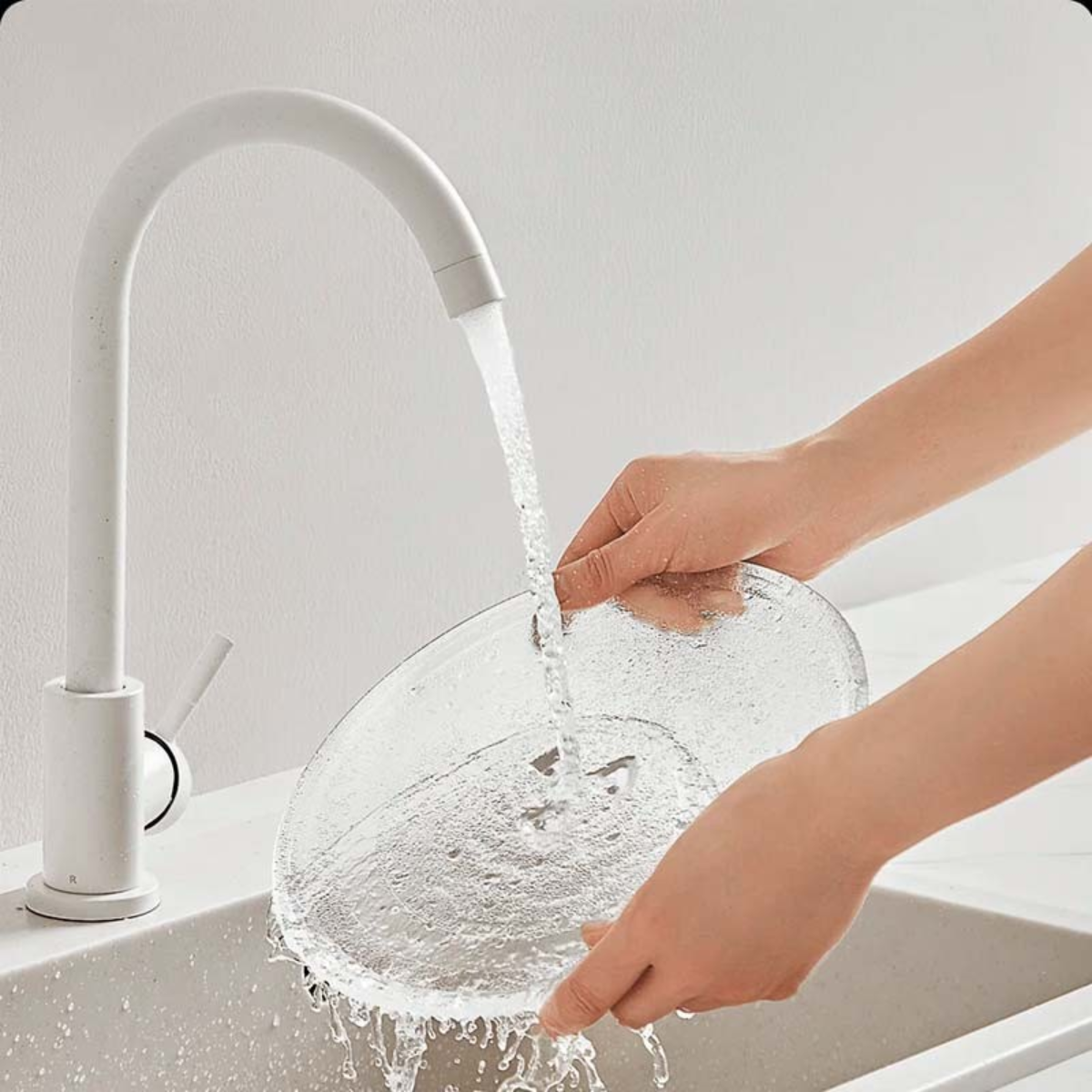 Biała bateria nalewa wodę do przezroczystej, teksturowanej miski trzymanej przez ręce w zlewie.