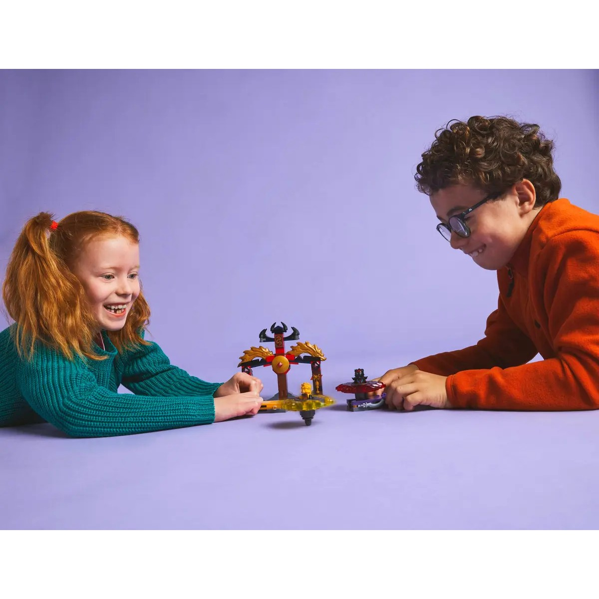Dos niños jugando con un set de Lego con un fondo morado.