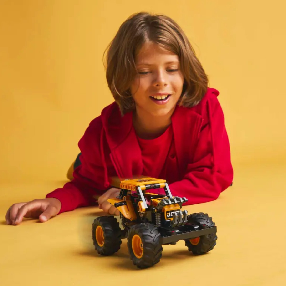 Un niño sonríe mientras mira un coche de juguete. Un fondo amarillo está detrás de él.