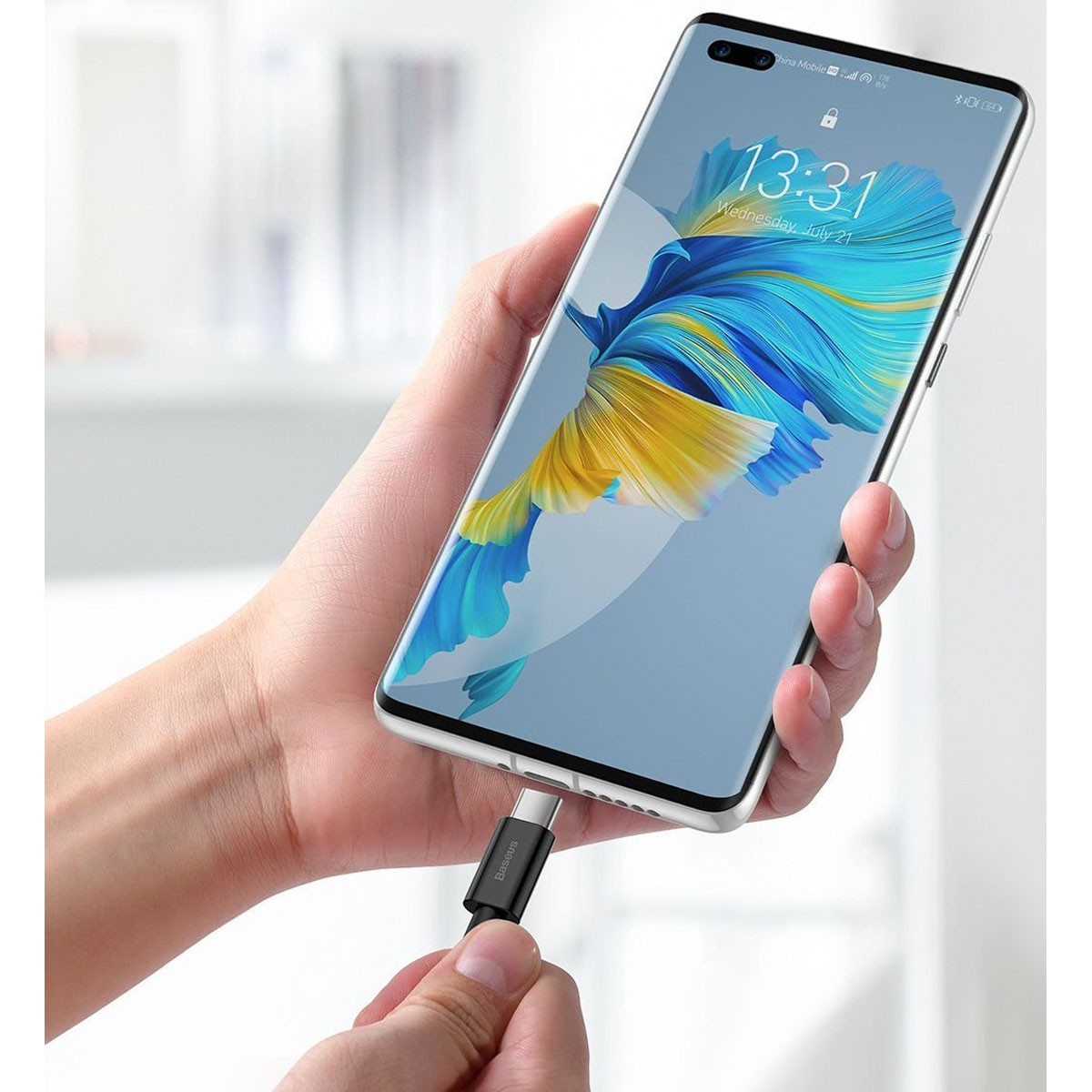 Ręka trzymająca czarny kabel USB-C podłączony do telefonu, białe tło.