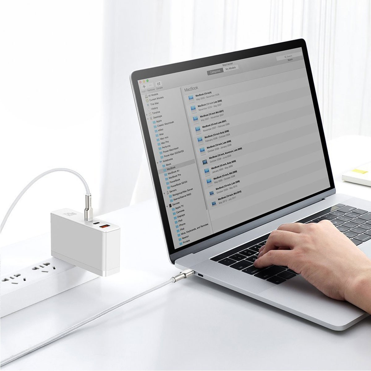 Portátil conectado a un adaptador de corriente mediante cable USB-C, en escritorio blanco.