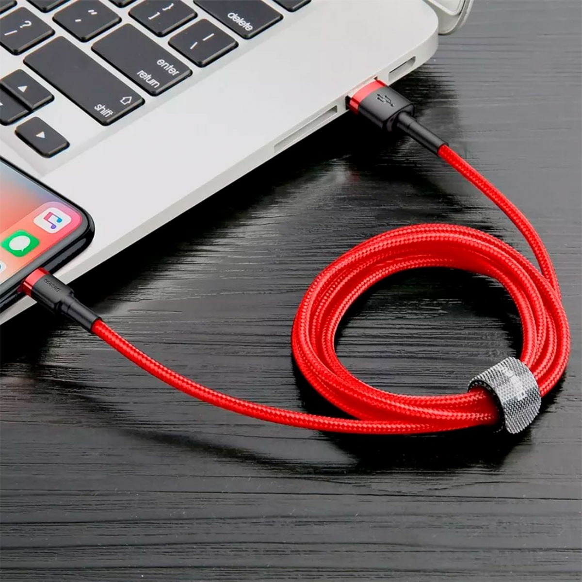 Czerwony kabel USB podłączony do telefonu i laptopa. Widoczny pasek marki Baseus.