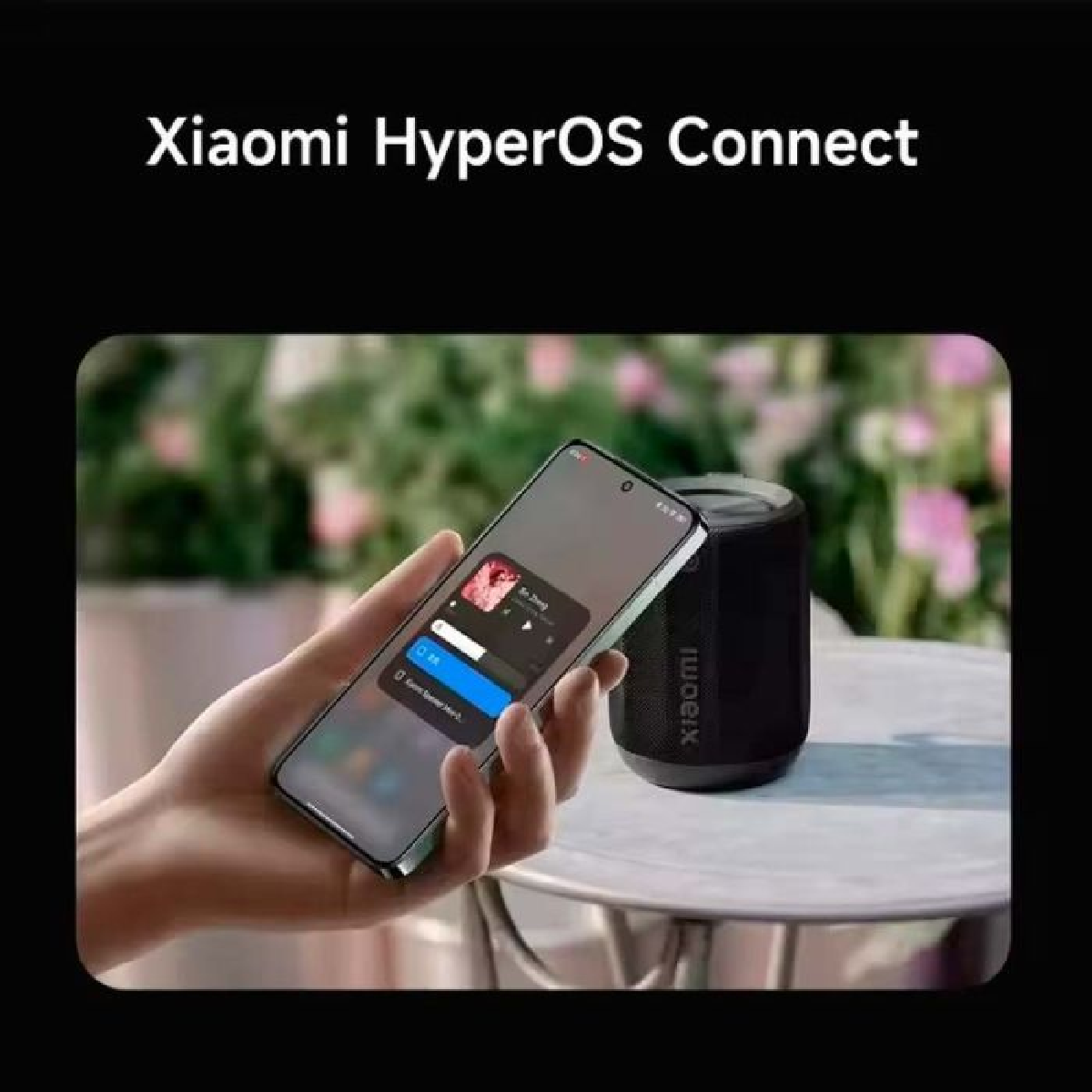 Eine Hand hält ein Telefon mit Benutzeroberfläche, neben einem schwarzen Lautsprecher.