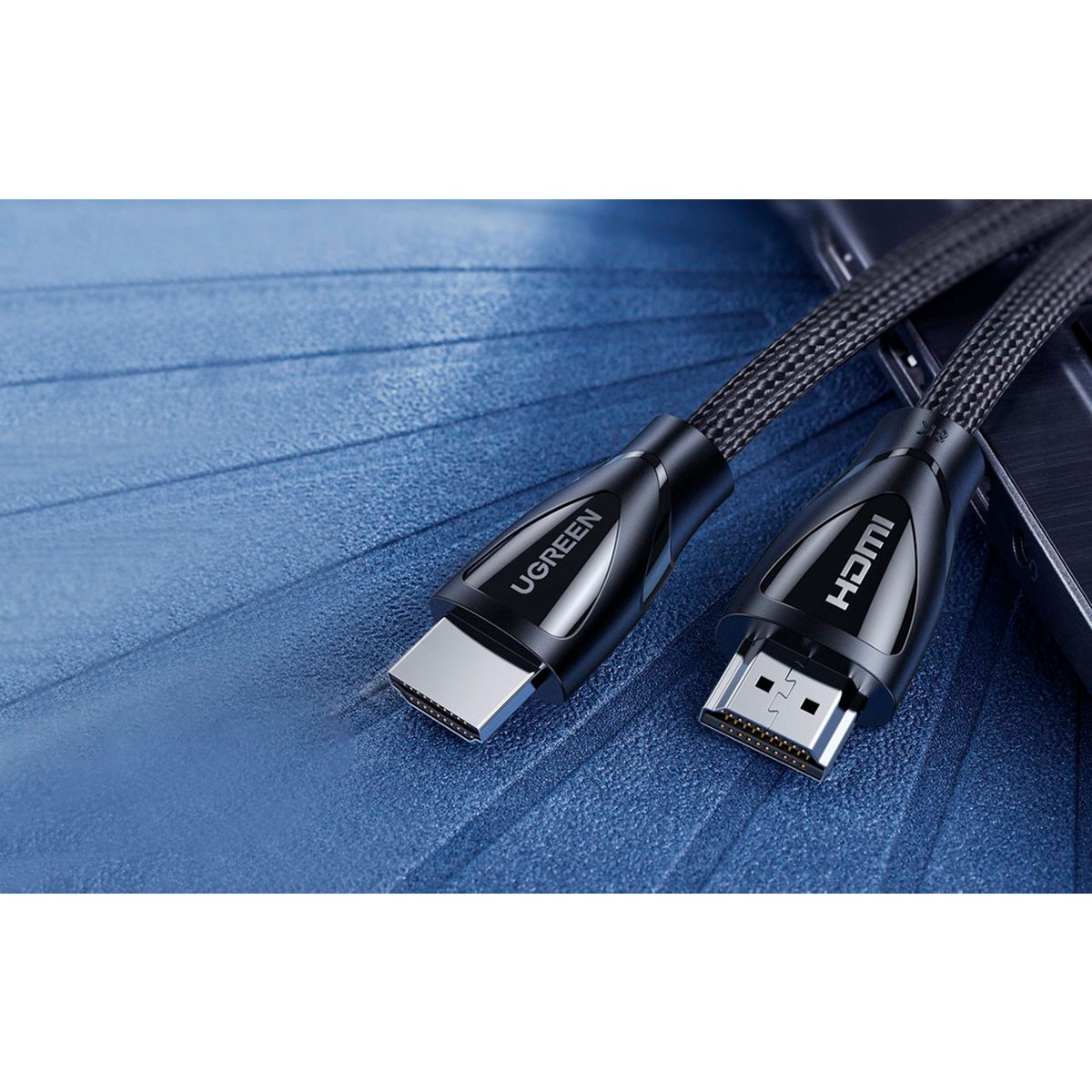 Kable HDMI UGREEN ze złączami. Kable są czarne ze srebrnymi złączami, leżące na niebieskiej powierzchni.