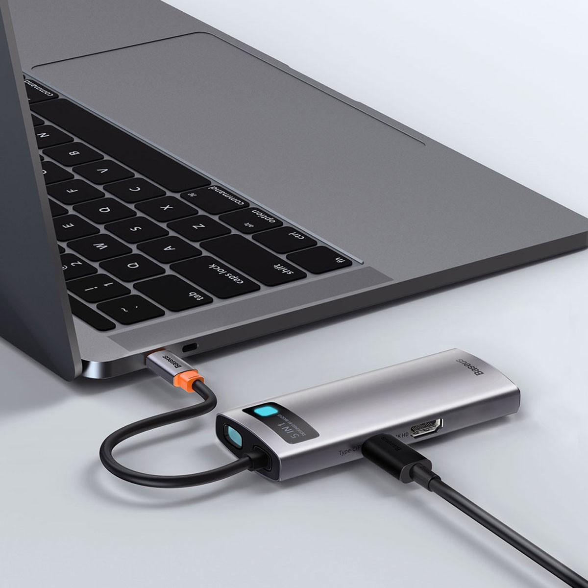 Laptop mit silbernem Hub mit mehreren Anschlüssen und schwarzem Kabel verbunden.