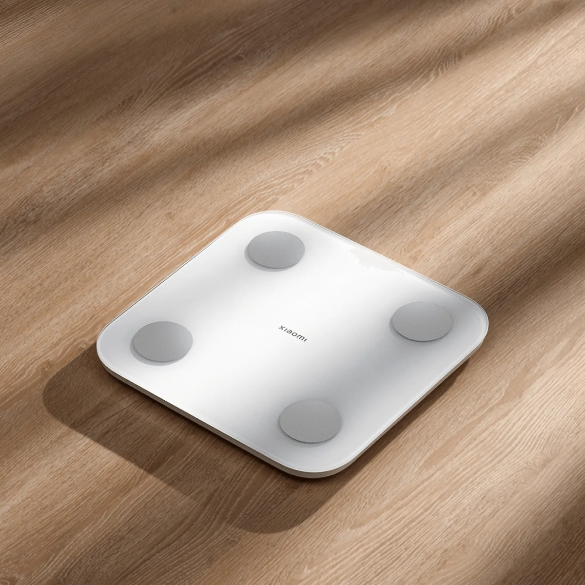 Biała inteligentna waga Xiaomi z czterema szarymi, okrągłymi podkładkami na drewnianej podłodze.