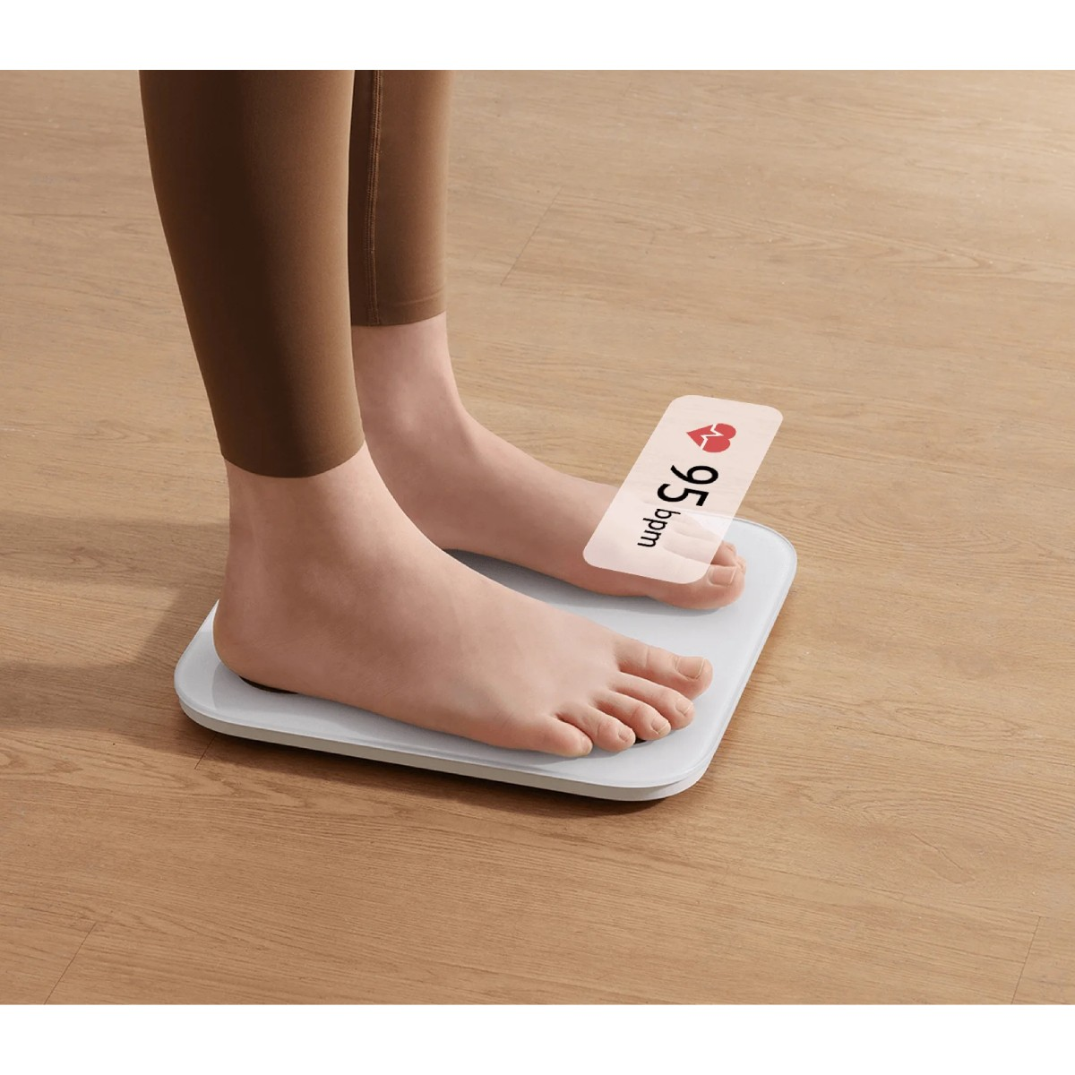 Stopy na białej wadze. Waga pokazuje tętno: 95 uderzeń na minutę. W tle drewniana podłoga.