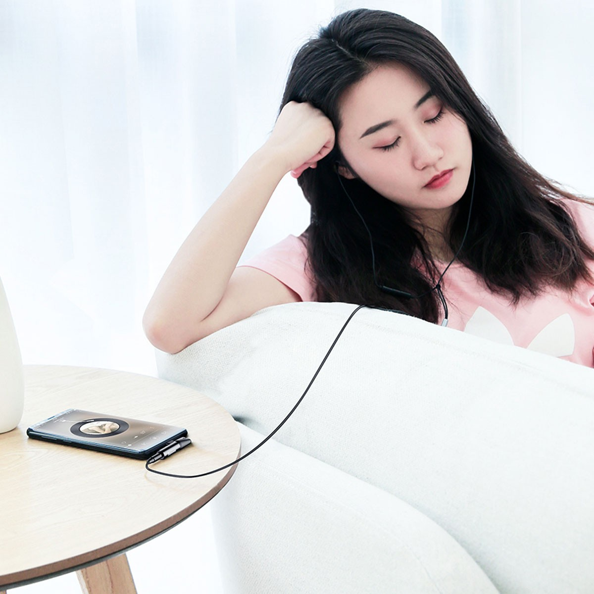 Kobieta siedzi i słucha muzyki na telefonie podłączonym czarnym przewodem.