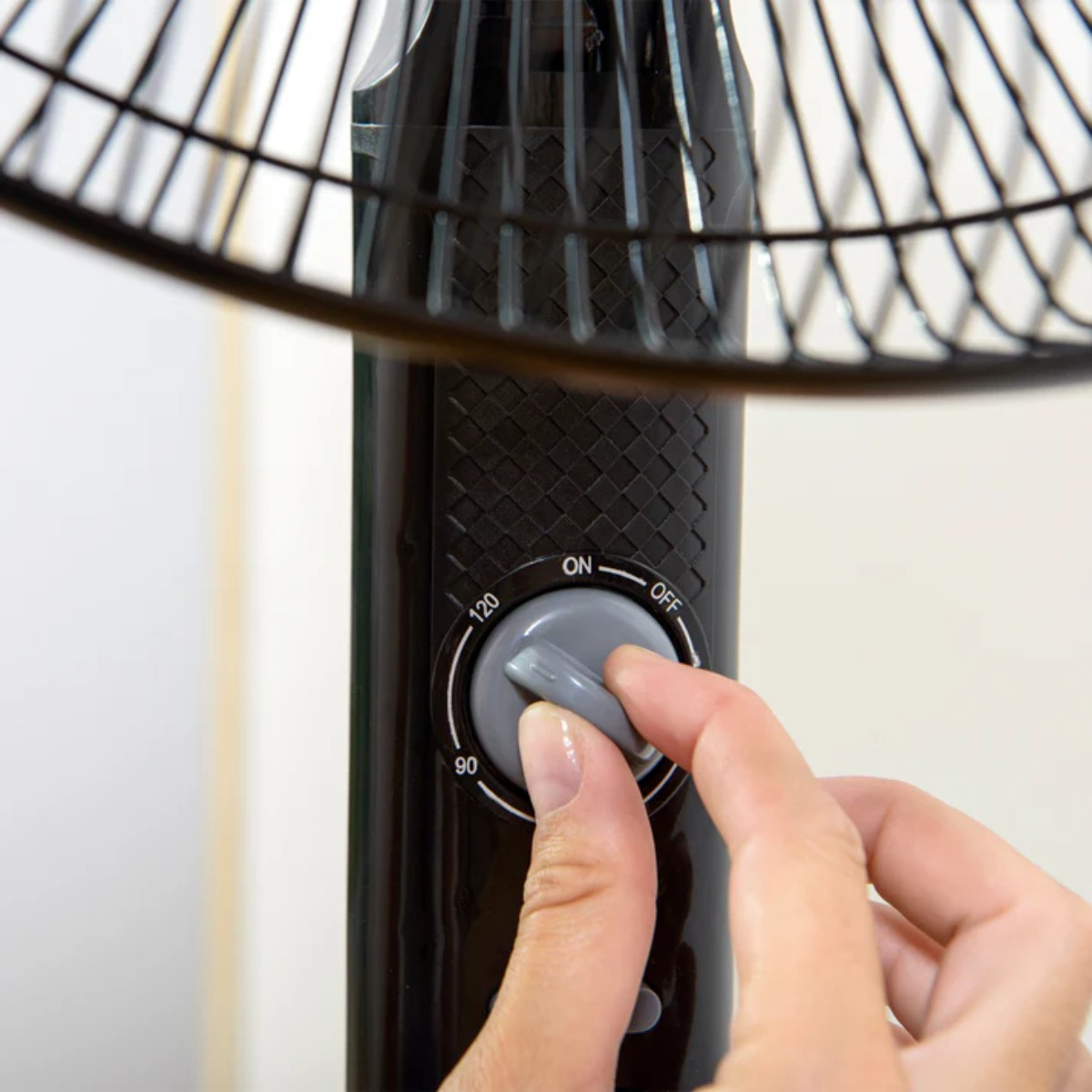 Ręka obracająca pokrętło na czarnym wentylatorze w celu dostosowania ustawienia oscylacji.
