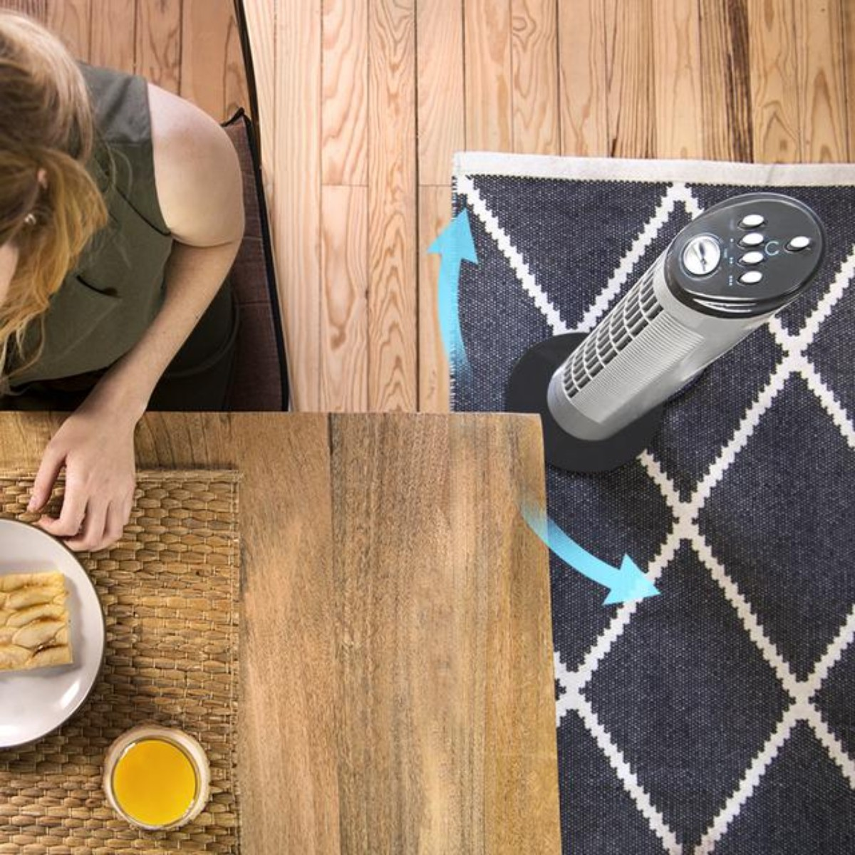 Kobieta jedząca przekąskę w pobliżu wentylatora na stole ze wzorzystym dywanem.