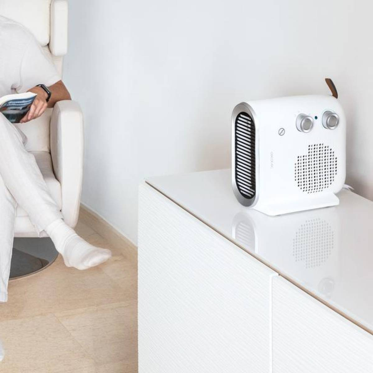 Termoventilatore bianco su un mobile bianco con una persona sullo sfondo seduta su una sedia bianca.