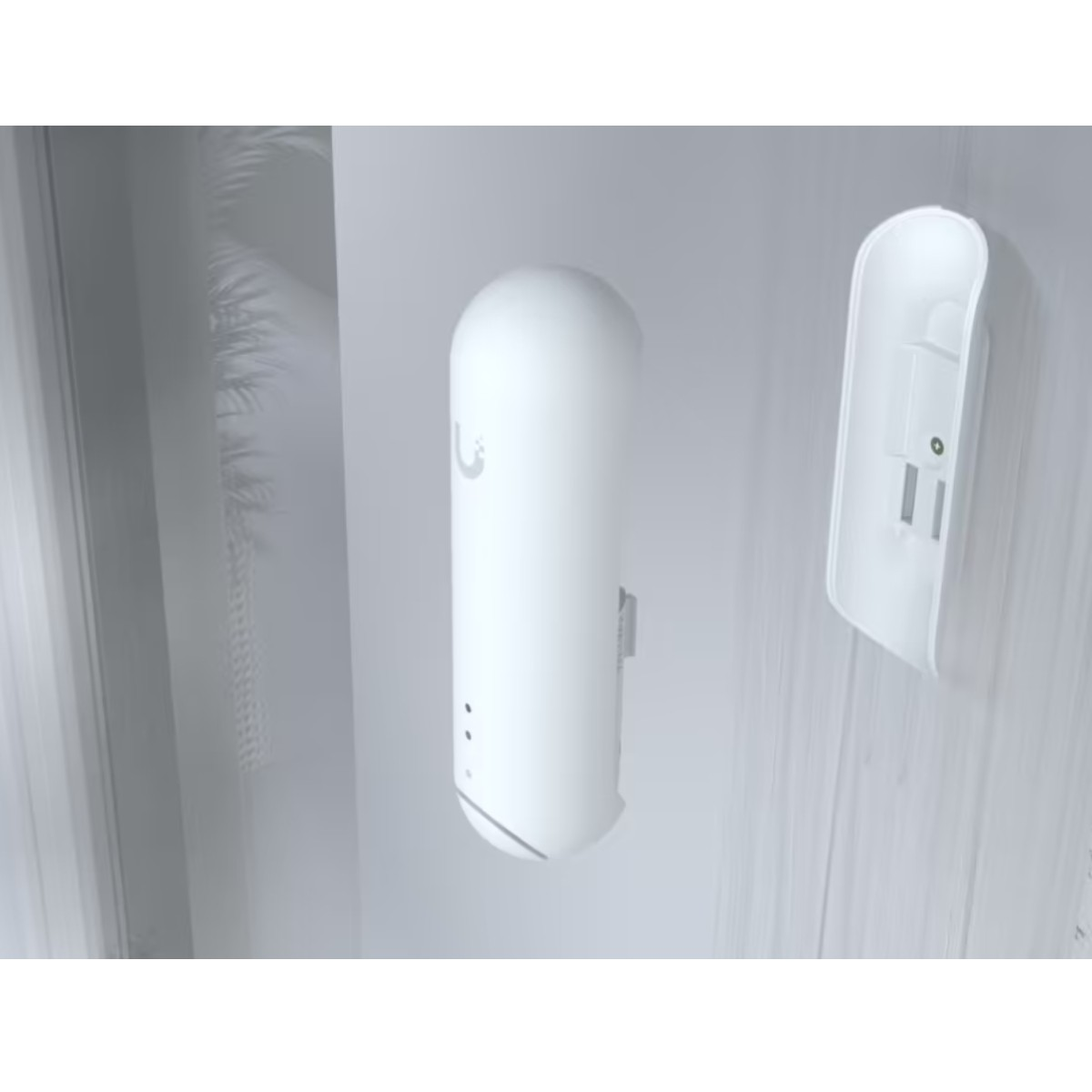 Dispositivo blanco montado en una pared, junto a su pieza de montaje.