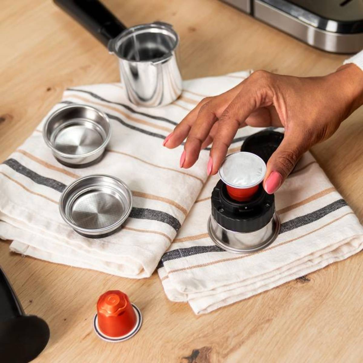 Dłoń umieszcza kapsułkę z kawą w maszynie. Części i kapsułki na drewnianej powierzchni.