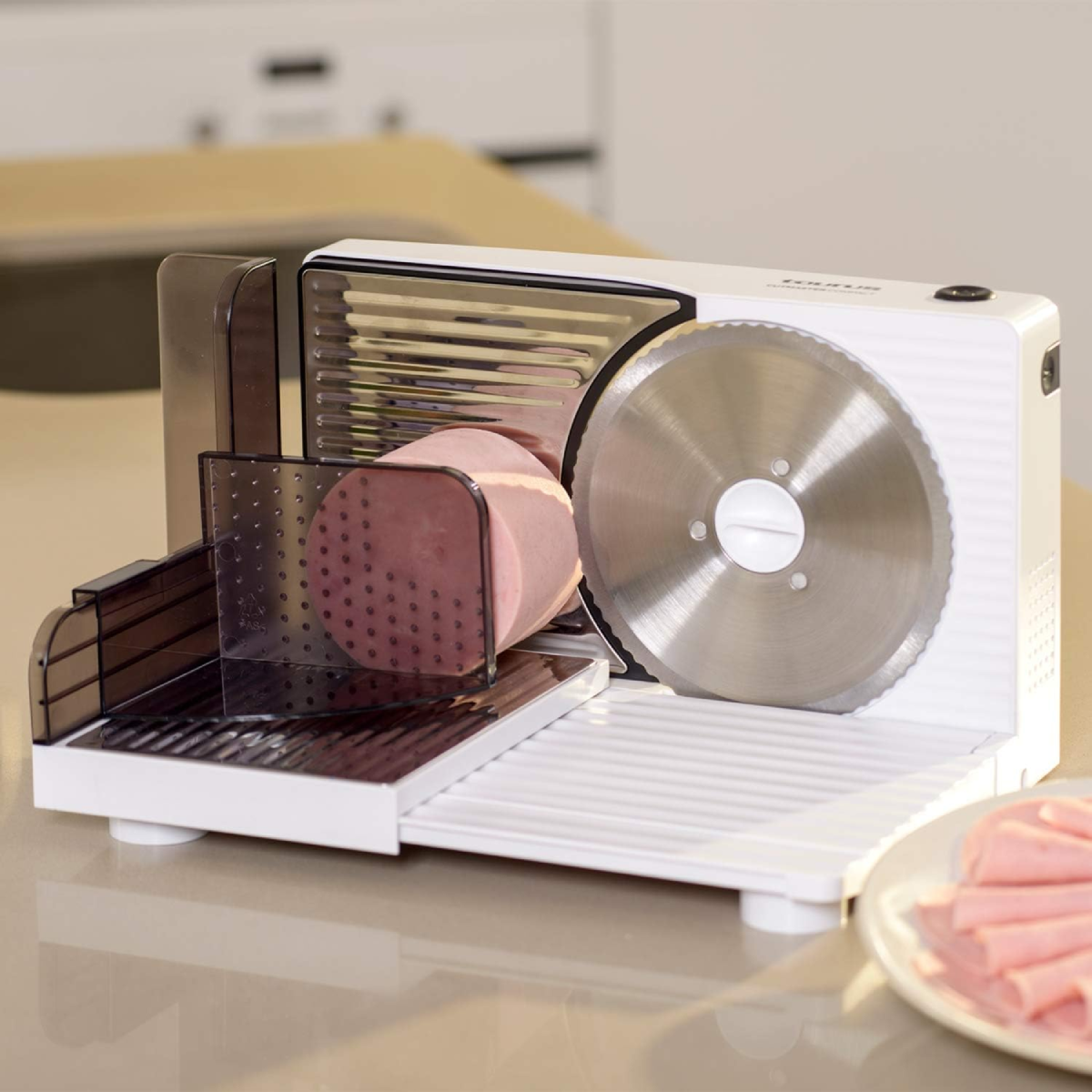 Un'affettatrice bianca che taglia il prosciutto. Prosciutto su un vassoio. Prosciutto affettato su un piatto sullo sfondo.