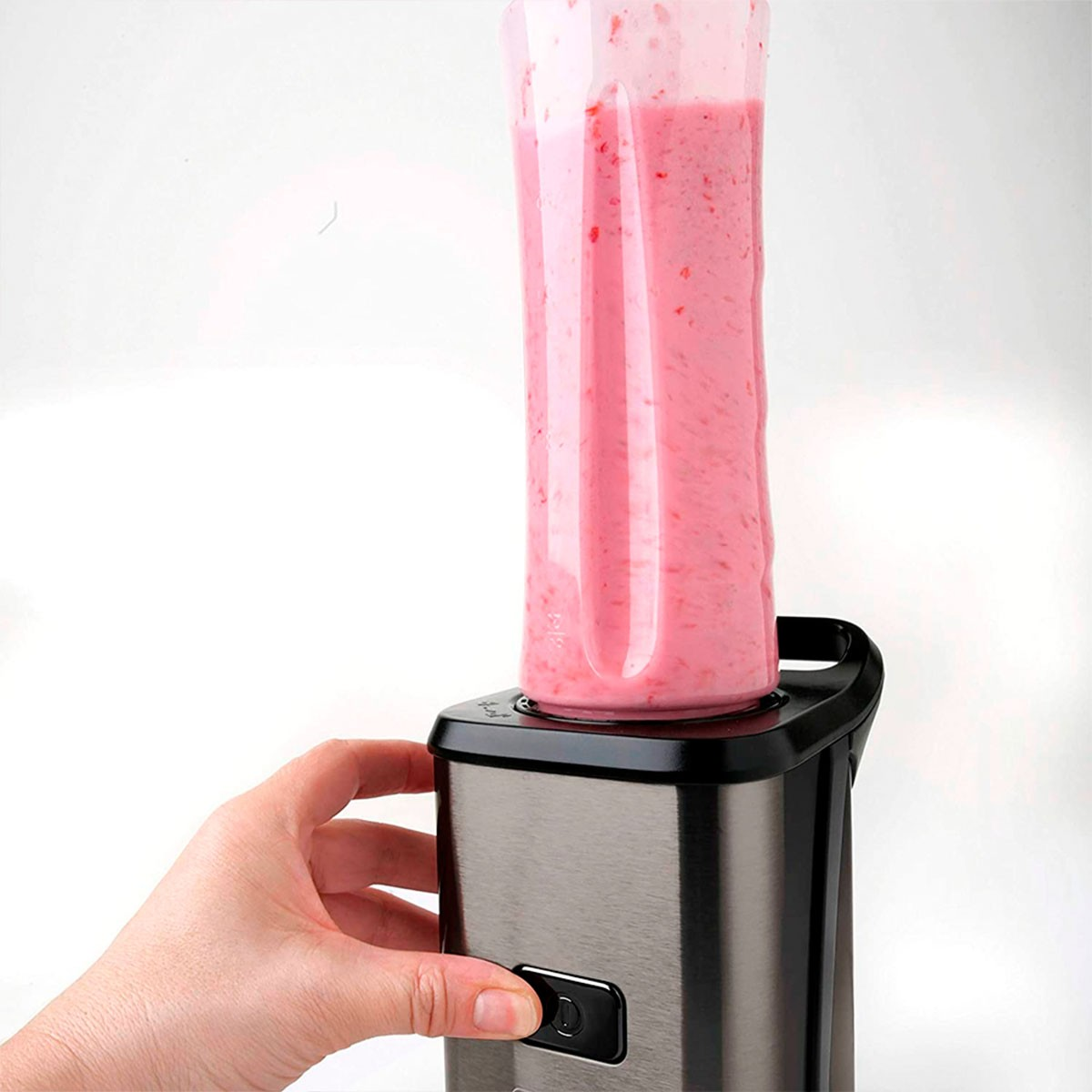 Mixer mit einem pinken Smoothie. Hand drückt einen Knopf auf dem Sockel. Weißer Hintergrund.