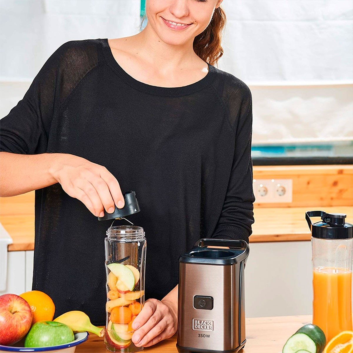 Frau gibt Zutaten in einen Mixer. Früchte in der Schüssel, fertiger Saft in einer klaren Flasche.