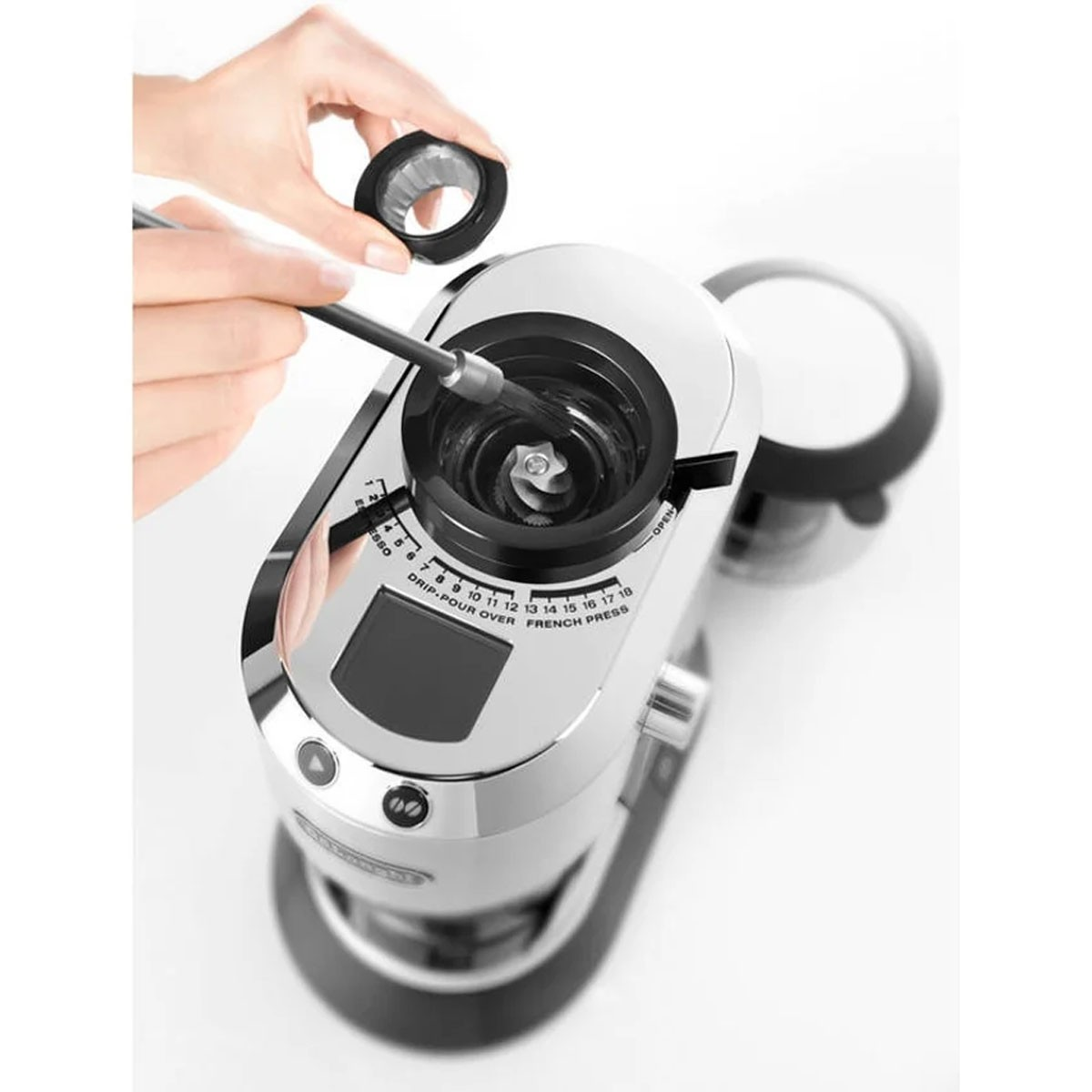 Ręka czyszcząca młynek do kawy. Młynek jest srebrny i czarny, na białym tle.