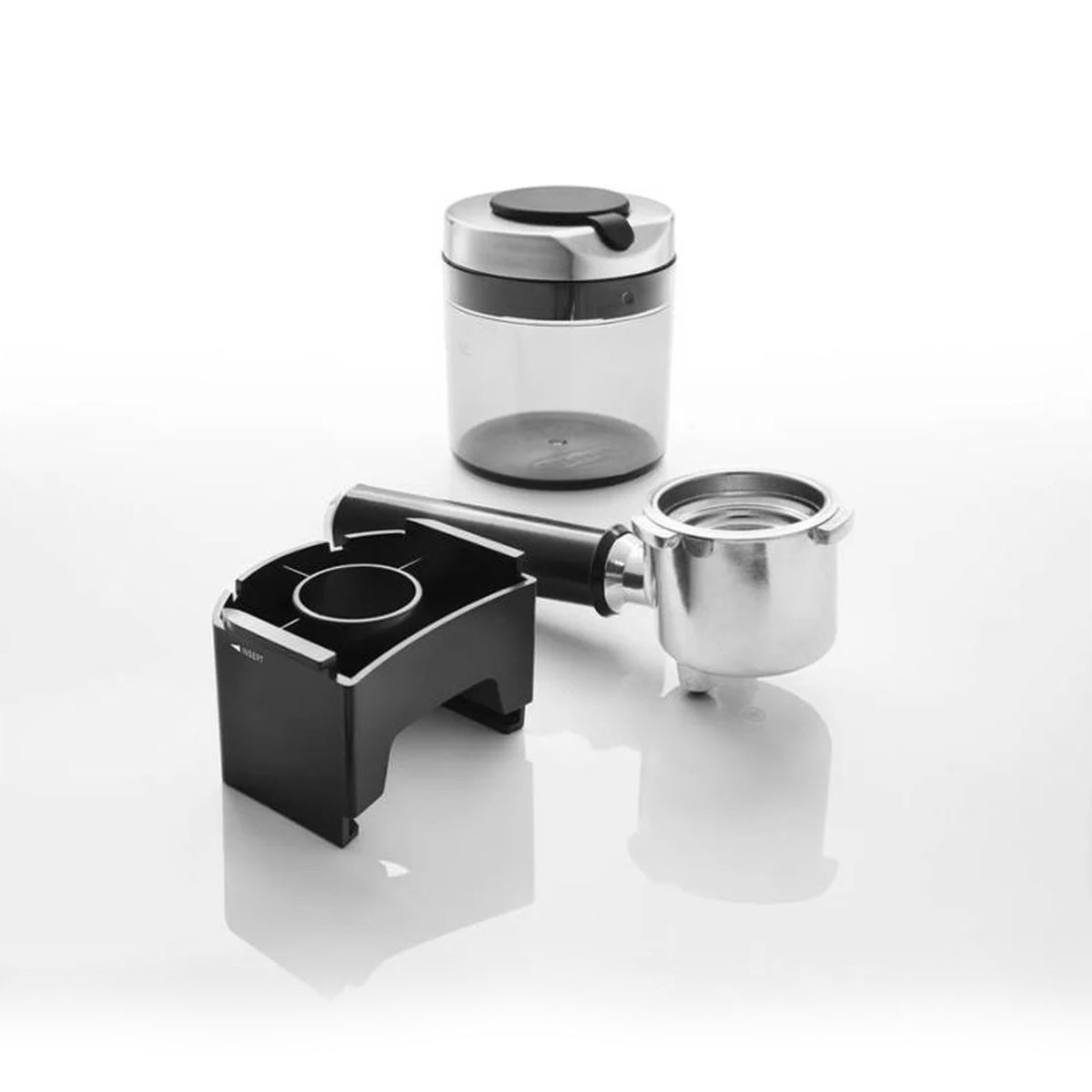 Czarne i srebrne części ekspresu do kawy: kolba, pojemnik i podstawa, na białym tle.