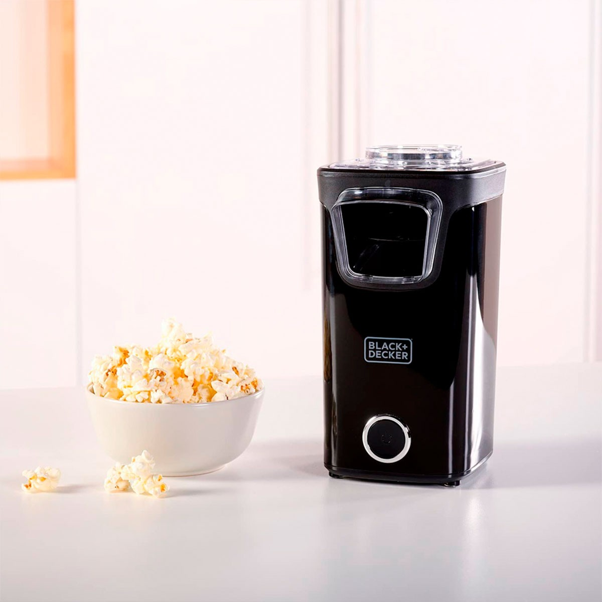 Maszyna do popcornu Black+Decker, miska popcornu i rozrzucony popcorn na białej powierzchni.