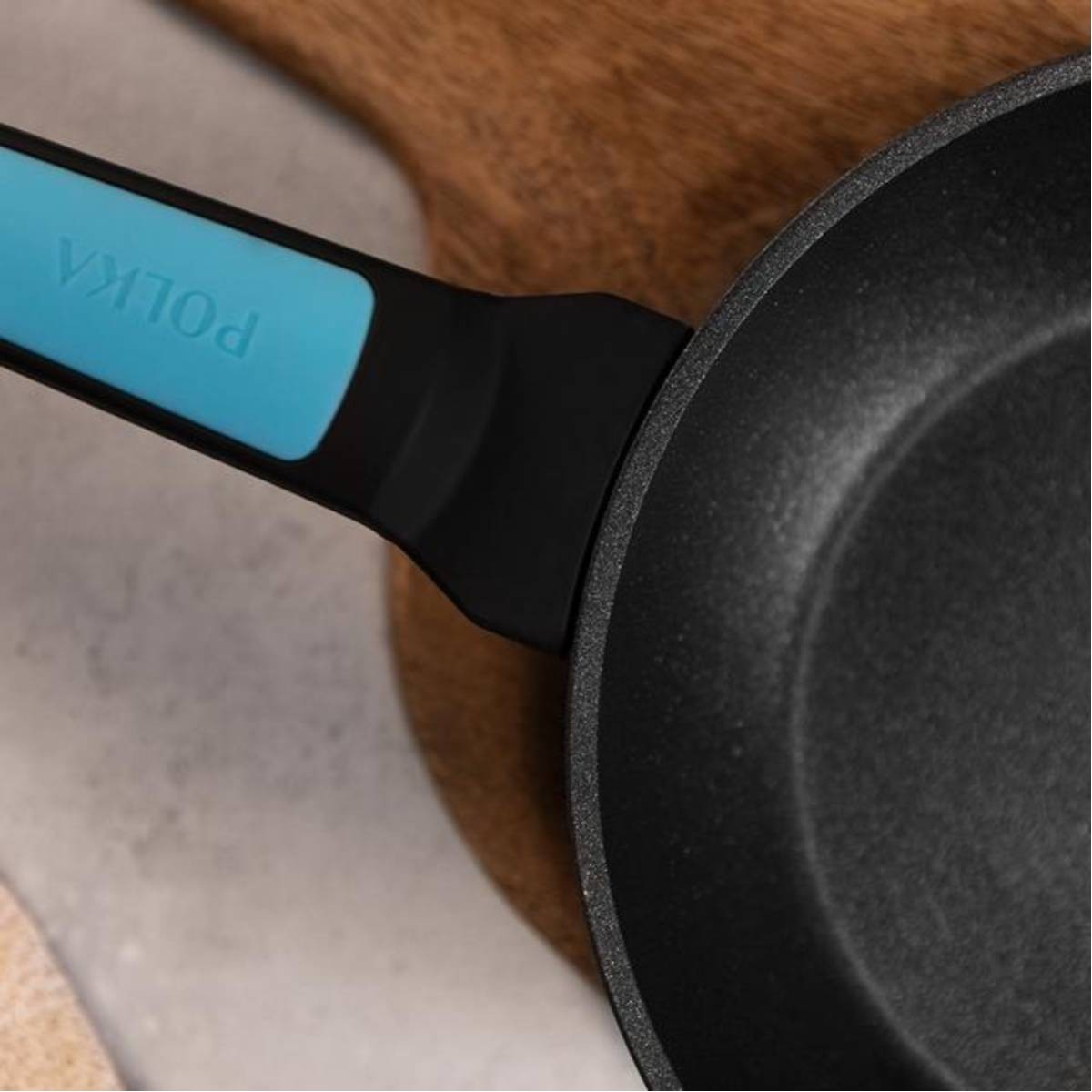 Zbliżenie czarnej patelni z niebieskim uchwytem na drewnianej powierzchni.