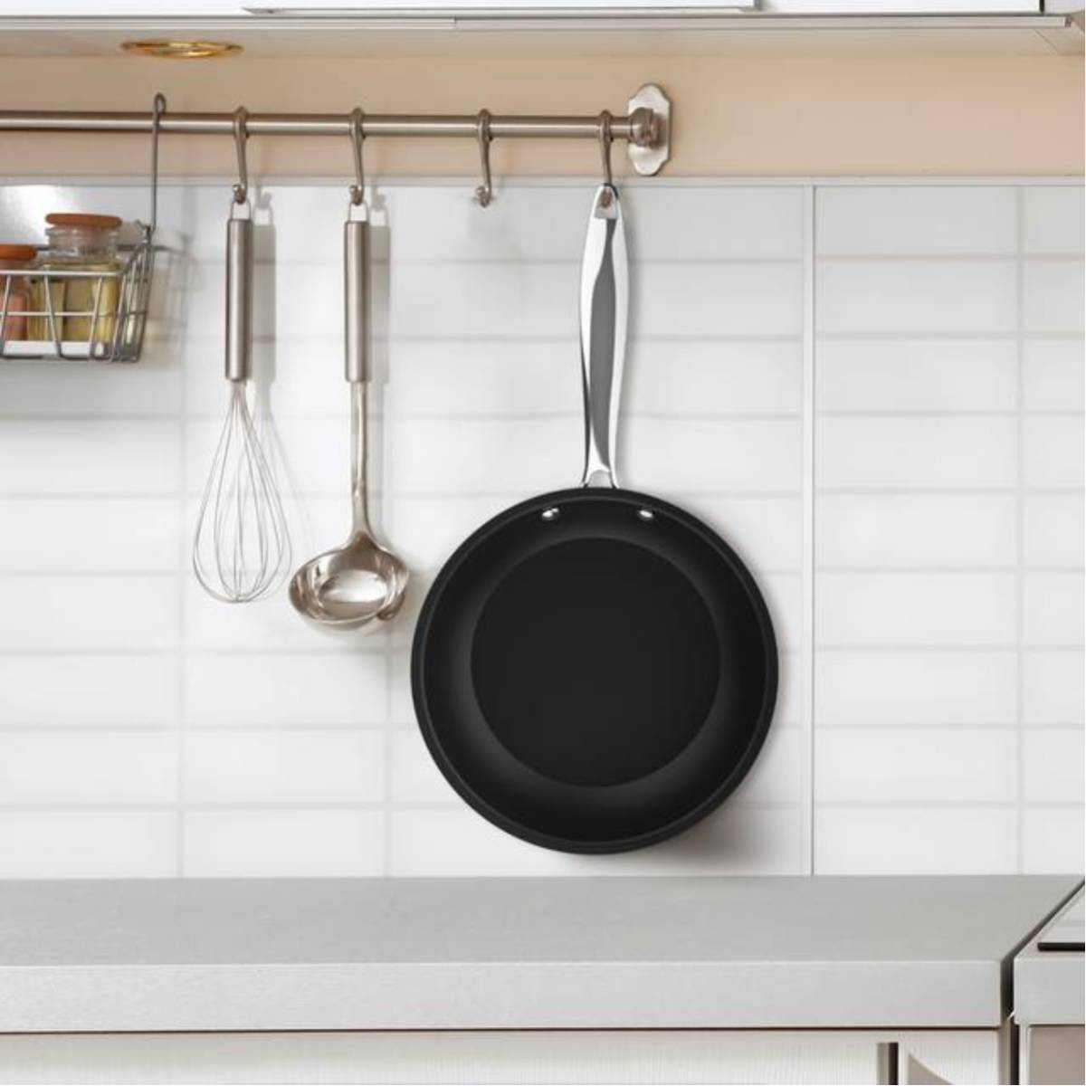 Keuken met een pan, garde en pollepel die aan een rail hangen. Witte tegelachtergrond.