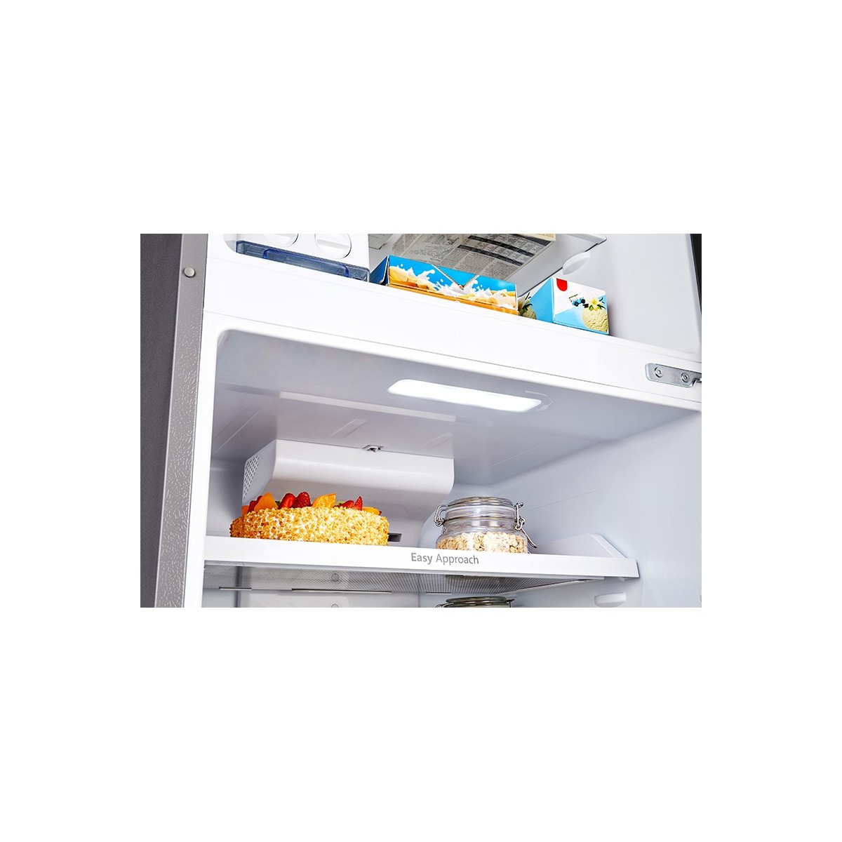 Zbliżenie wnętrza lodówki z półkami, ciastem i innymi przedmiotami.