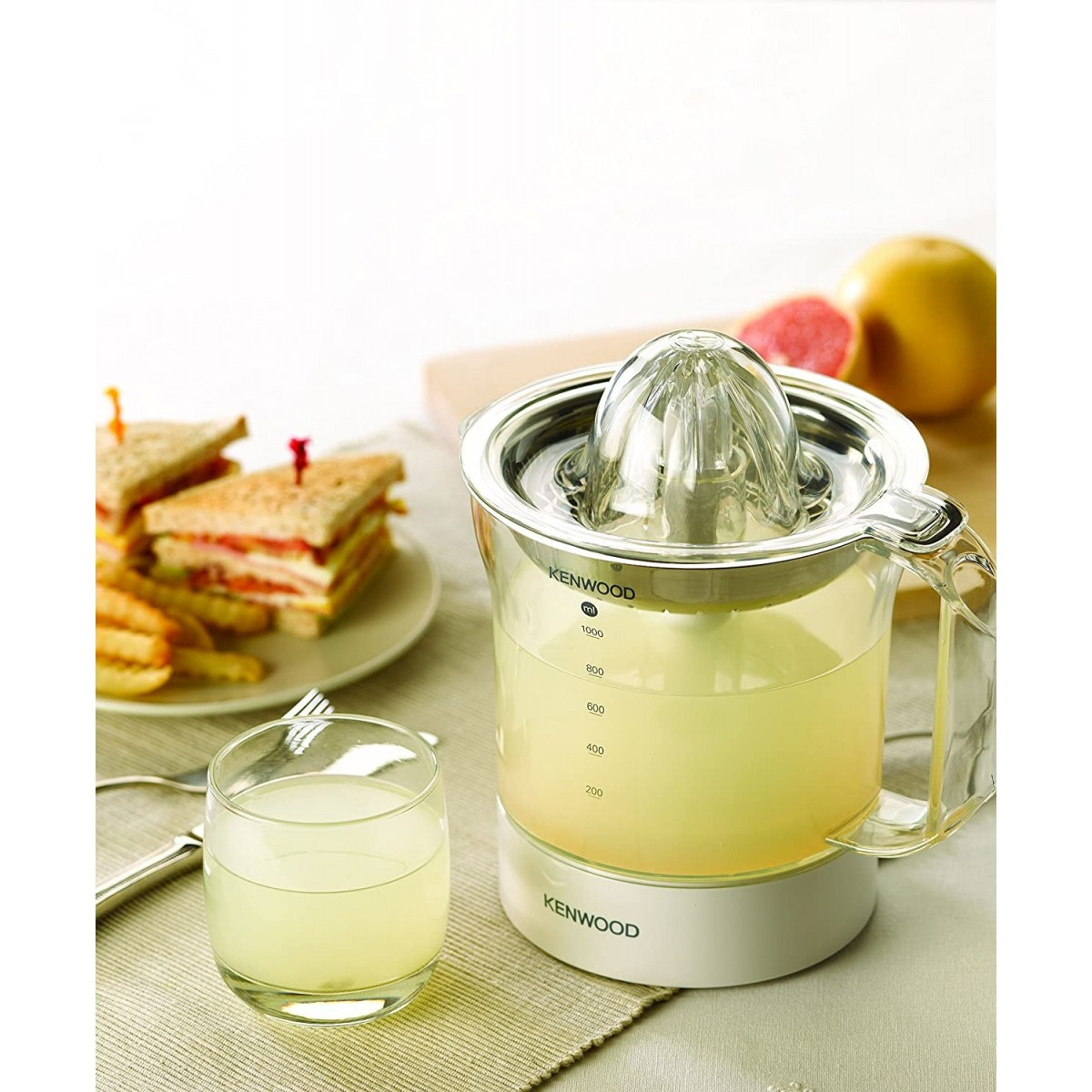 Wyiskarka z sokiem, kanapkami i szklanką. Scena ma jasną paletę kolorów.