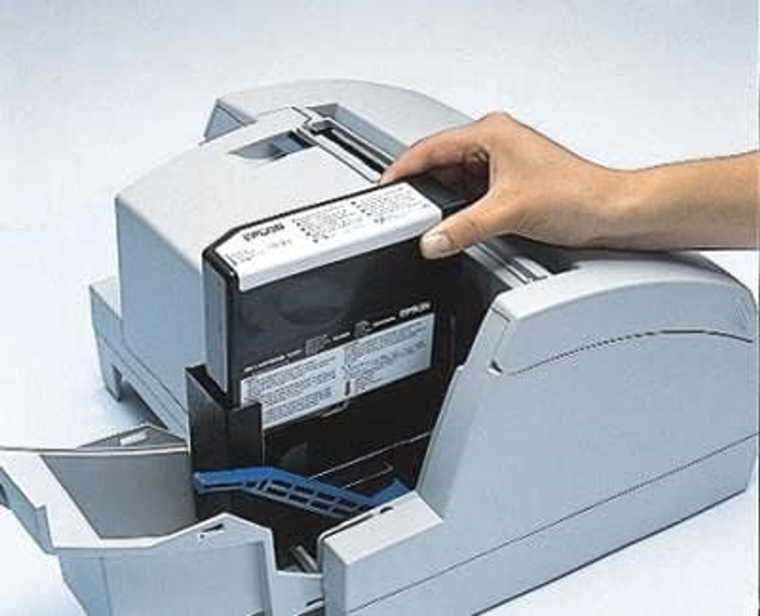 Mano instalando un nuevo cartucho de impresora en una impresora. La impresora es gris claro.
