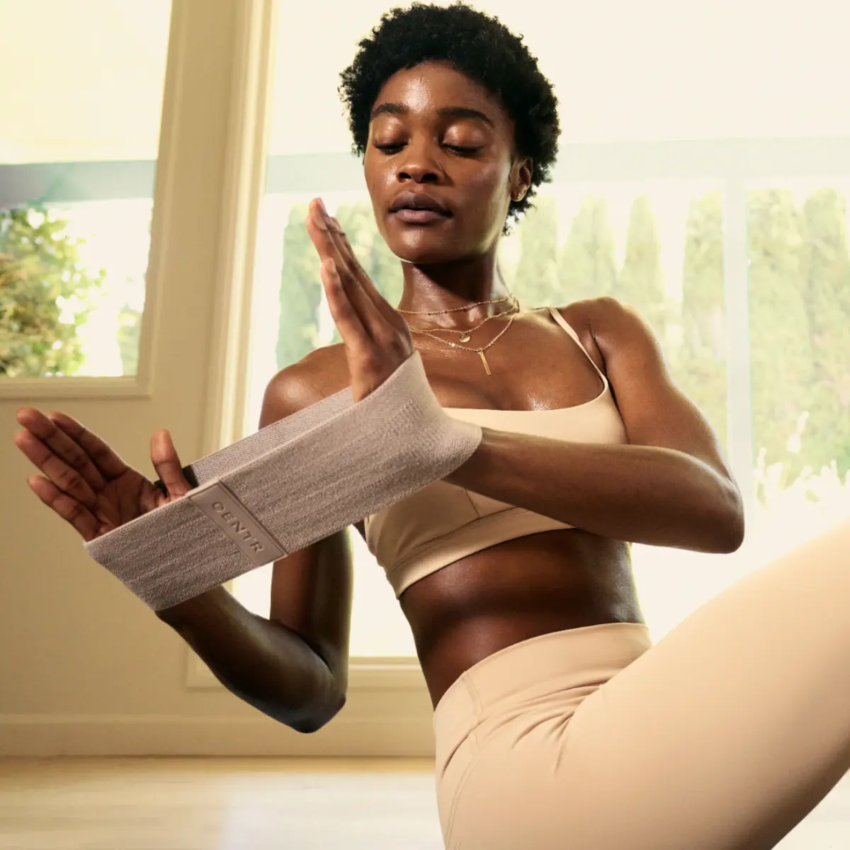 A woman is working out with a resistance band, sitting on the floor with closed eyes.