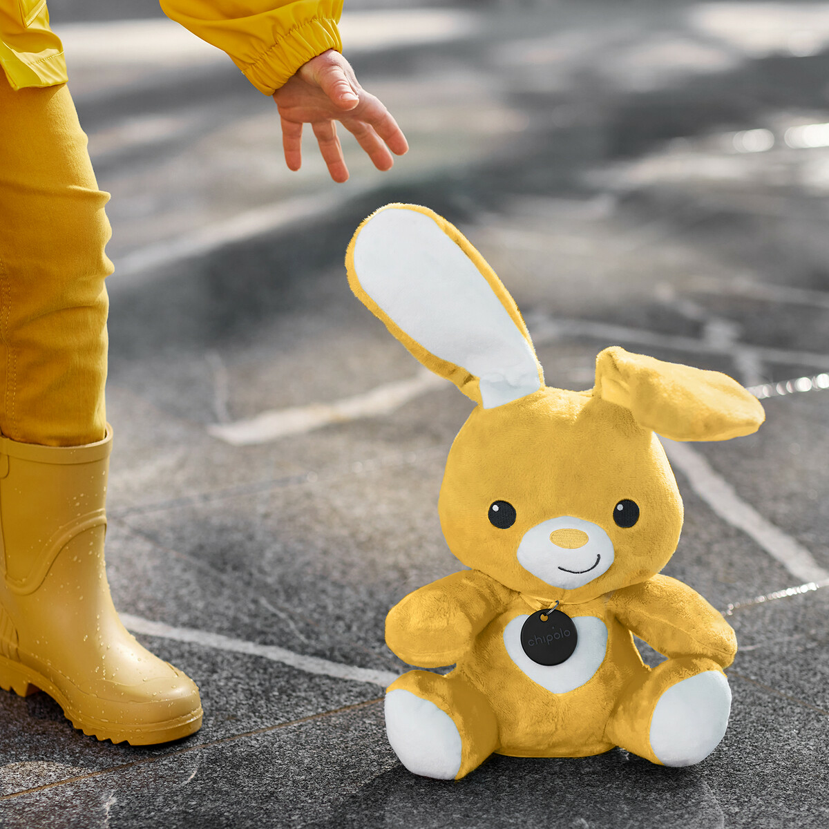 A child in yellow clothing reaching for a yellow bunny toy on a wet surface.