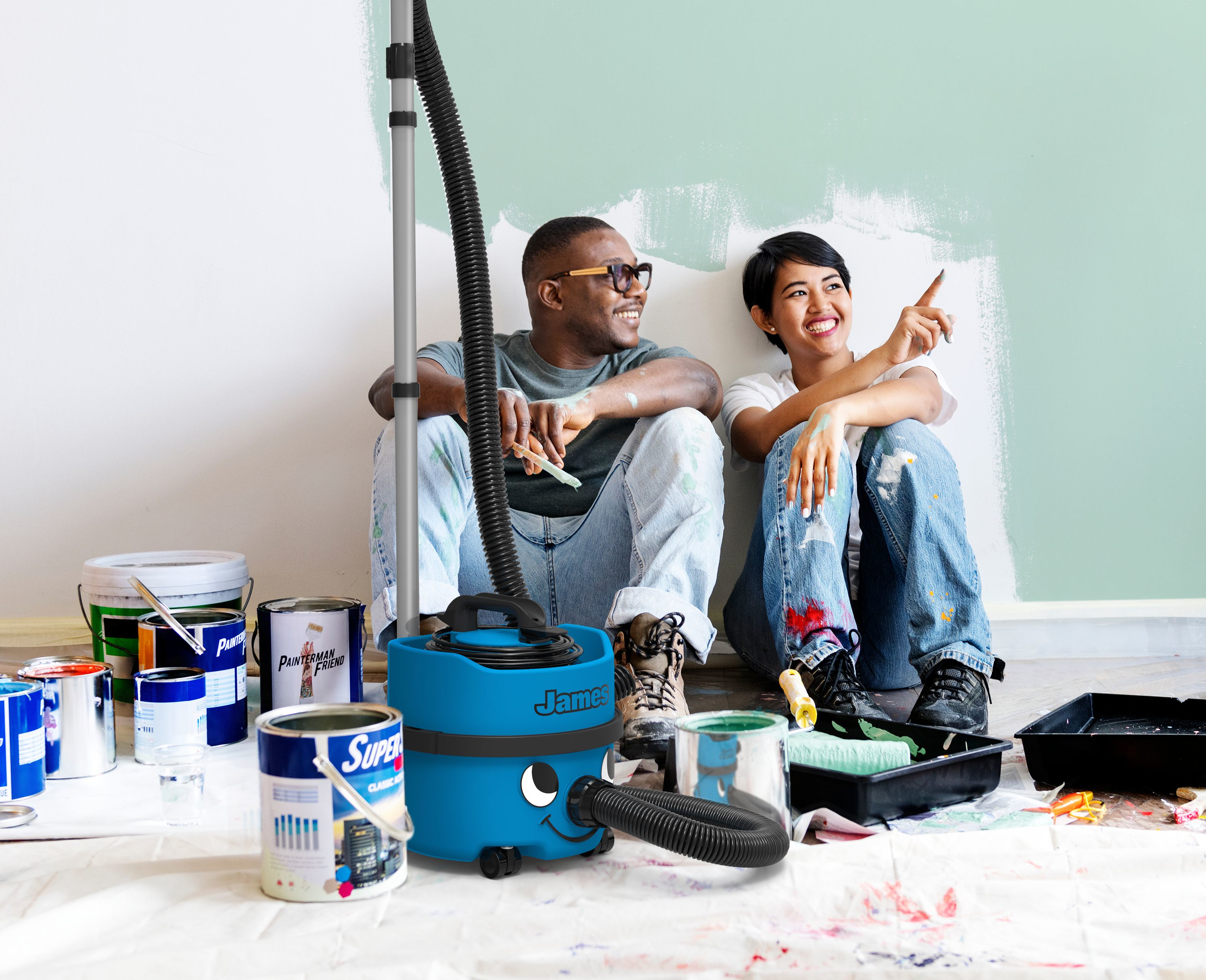 A man and woman paint, with a blue vacuum cleaner and paint supplies.