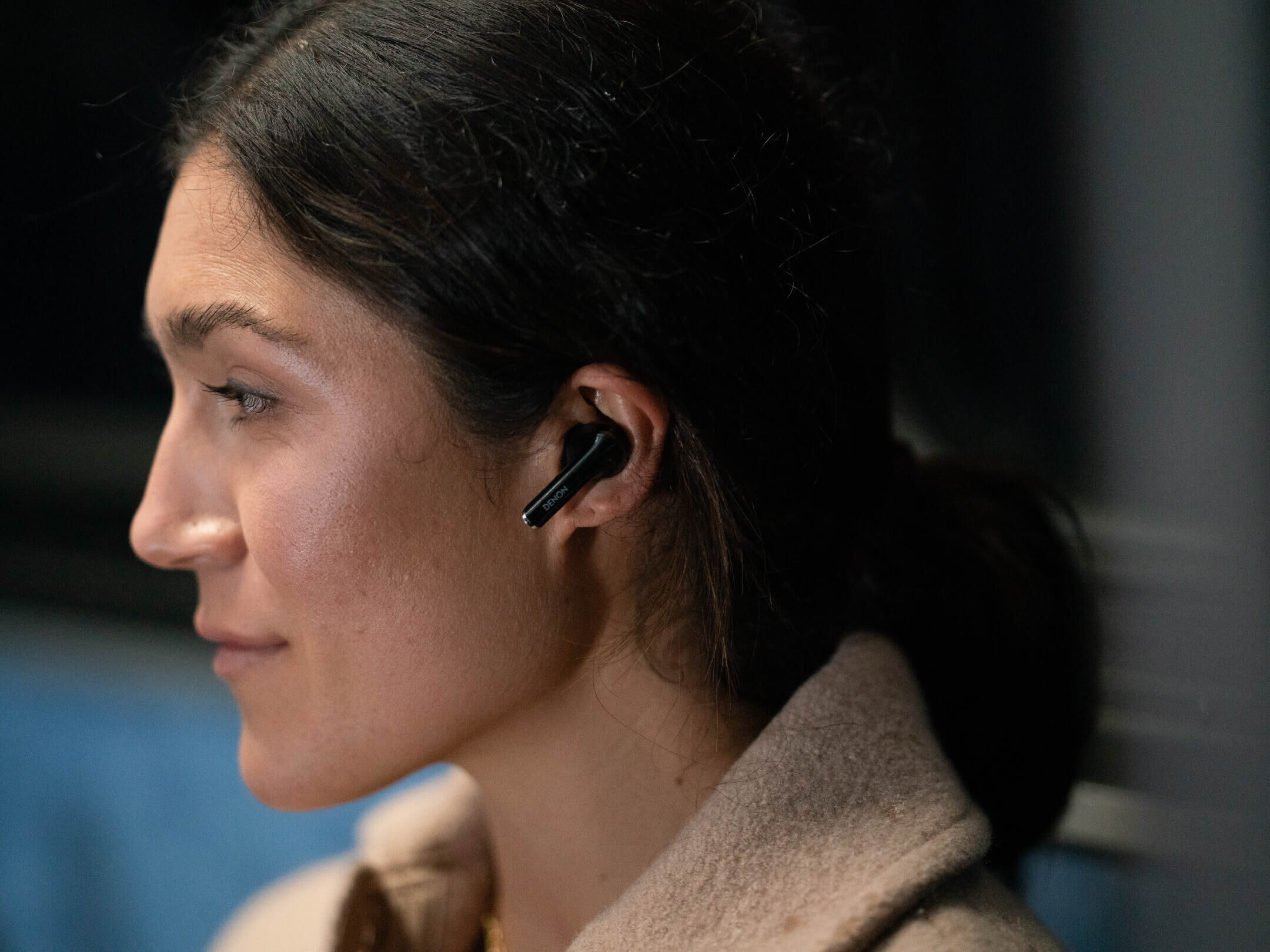 Kobieta nosząca słuchawkę Denon w uchu. Słuchawka ma srebrną końcówkę. Patrzy w bok.