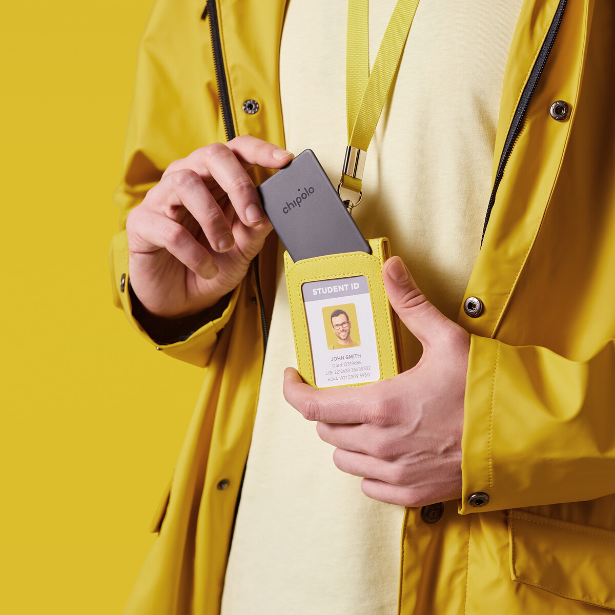 Person holding a yellow ID holder with student ID, and gray Chipolo tracker.
