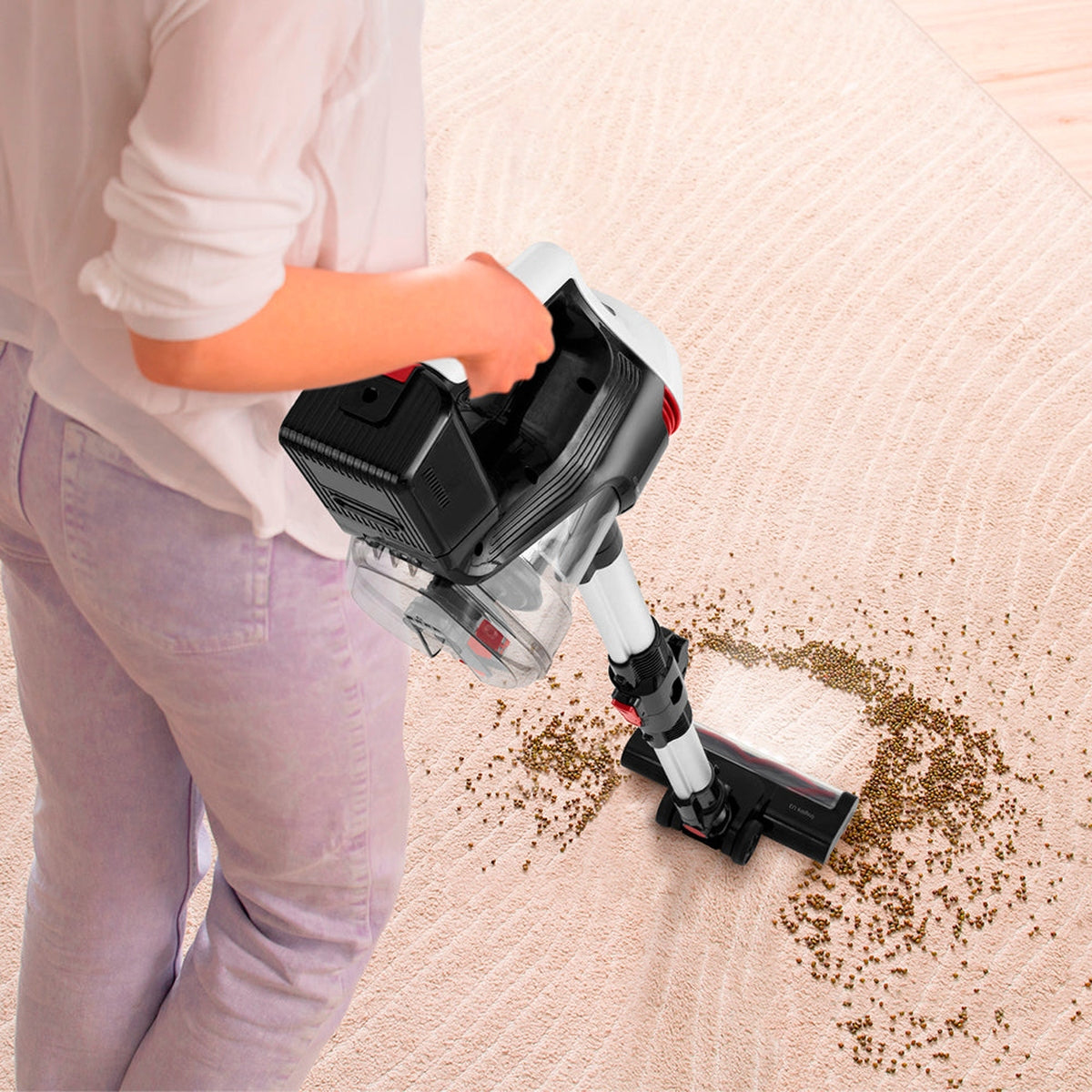 Una persona aspirando una alfombra. La aspiradora es blanca y negra con un detalle rojo. La alfombra es beige.