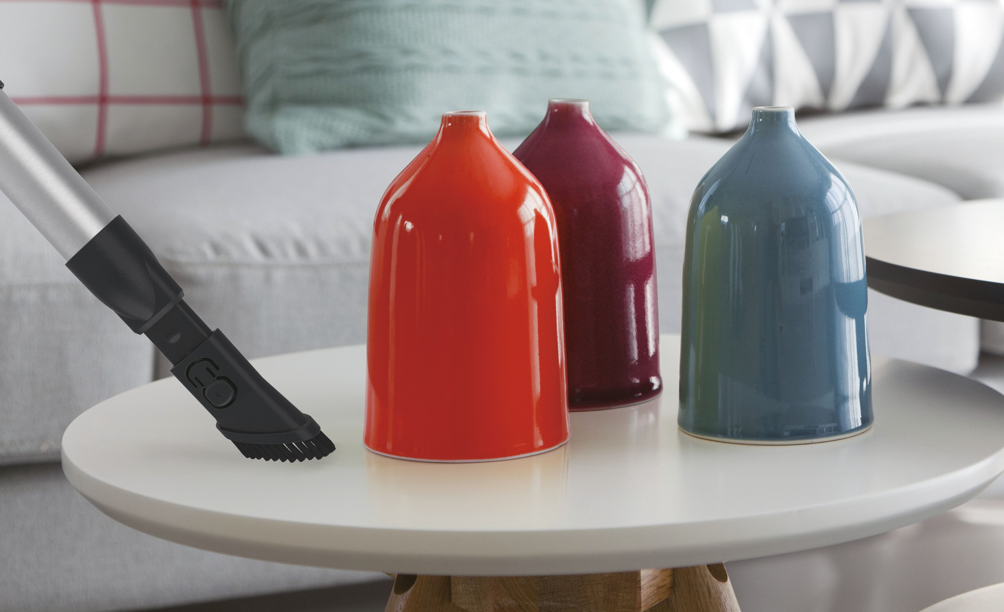 Odkurzacz czyszczący stół z kolorowymi wazonami.