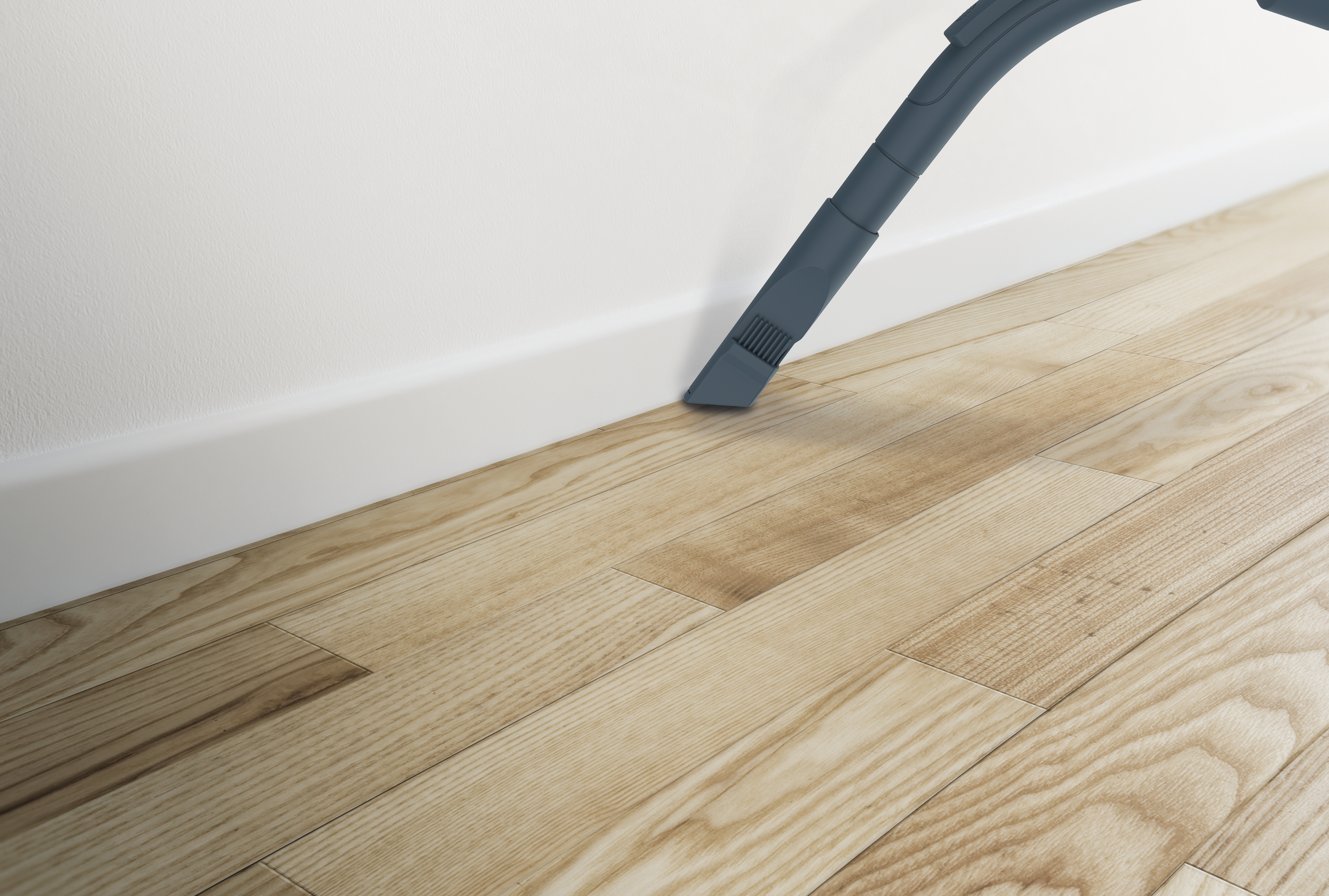 Dysza odkurzacza czyszcząca drewnianą podłogę obok białej listwy przypodłogowej.