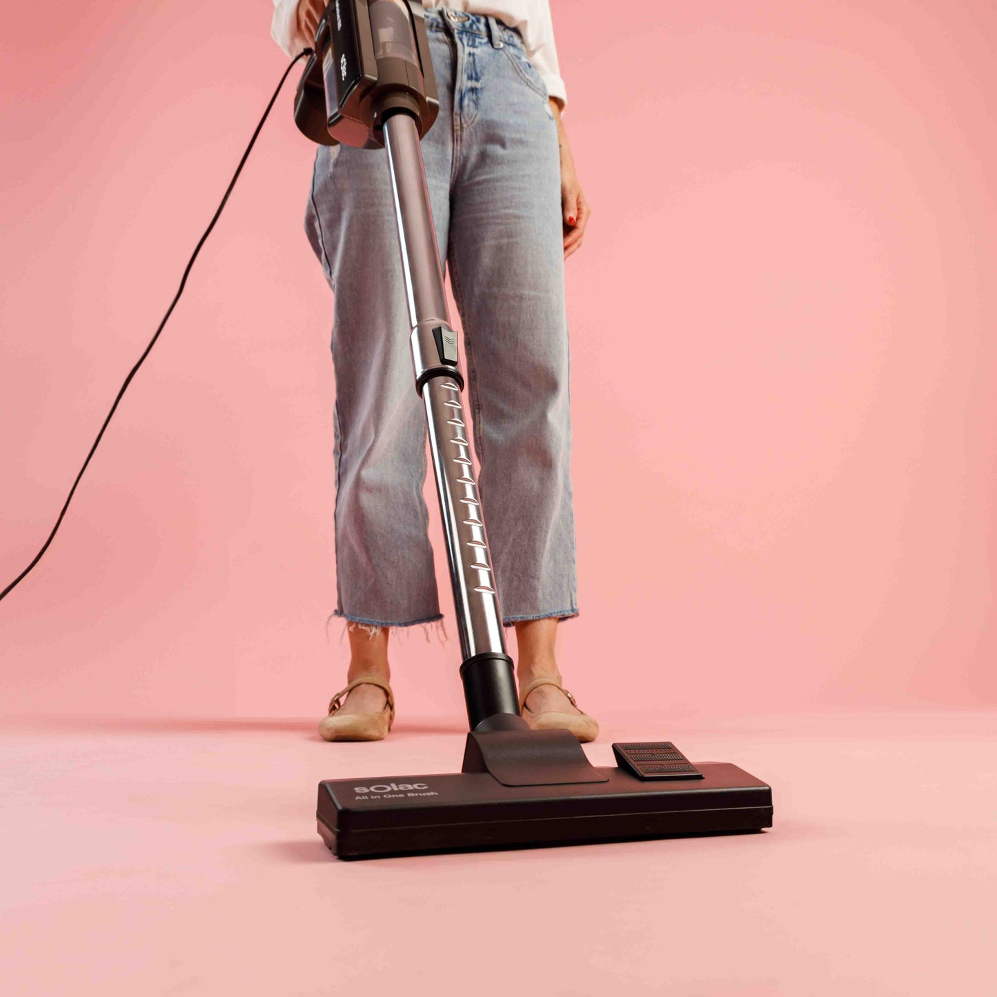 Osoba odkurzająca czarno-srebrnym odkurzaczem Solac. Różowe tło.