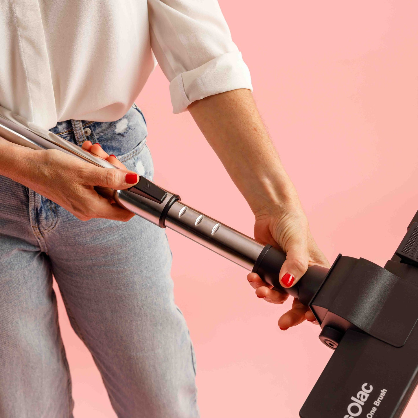 Dłonie trzymające srebrną rurę od odkurzacza. Czerwony lakier do paznokci i różowe tło.