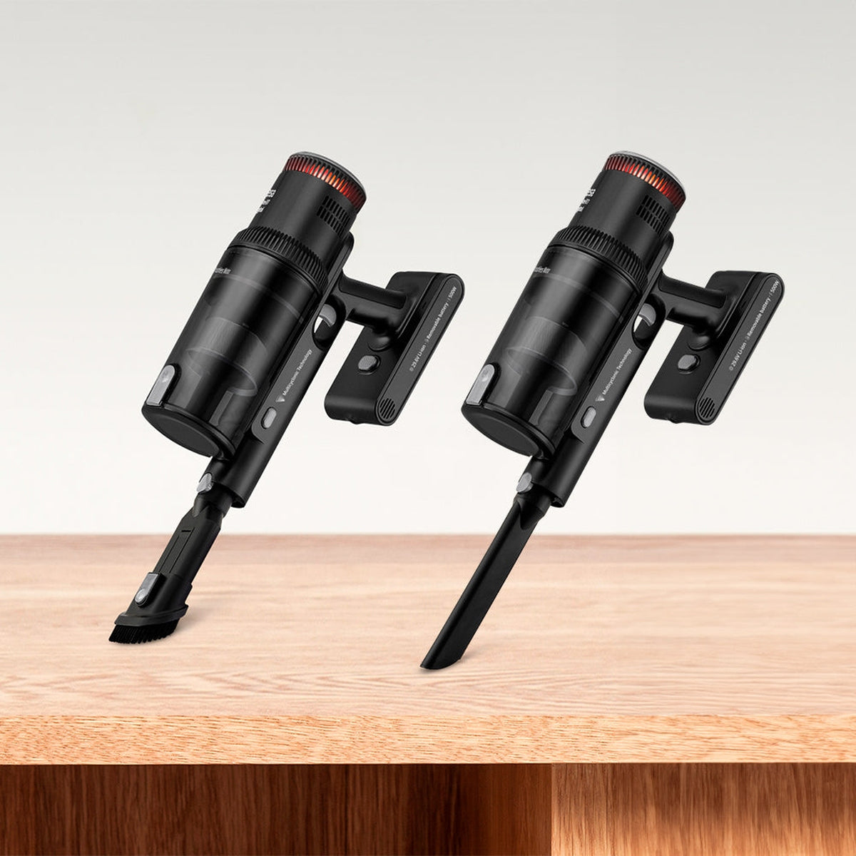 Dos aspiradoras inalámbricas negras con luces rojas. Están sobre una mesa de madera.