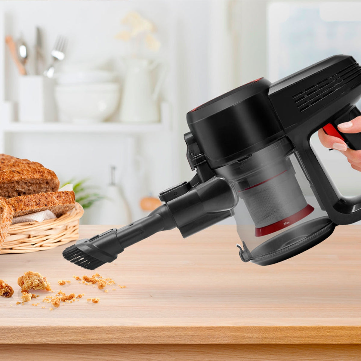 Una persona usa una aspiradora inalámbrica. Se limpian migas de pan en una mesa de madera.