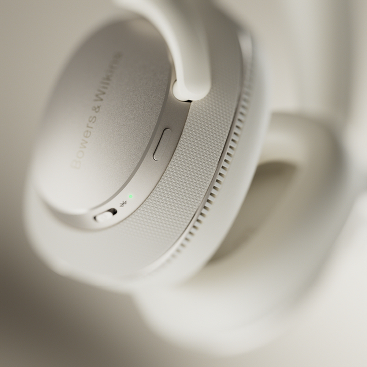 Białe słuchawki Bowers & Wilkins. Widoczna prawa słuchawka z przyciskiem i zielonym światłem.
