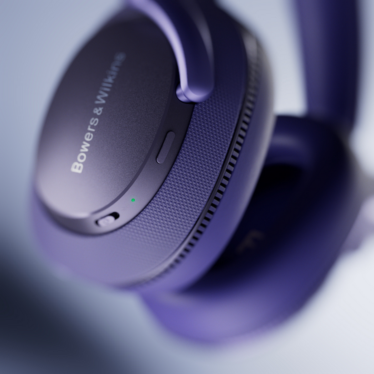 Auriculares morados con el logo de Bowers & Wilkins. Primer plano, una luz verde visible.