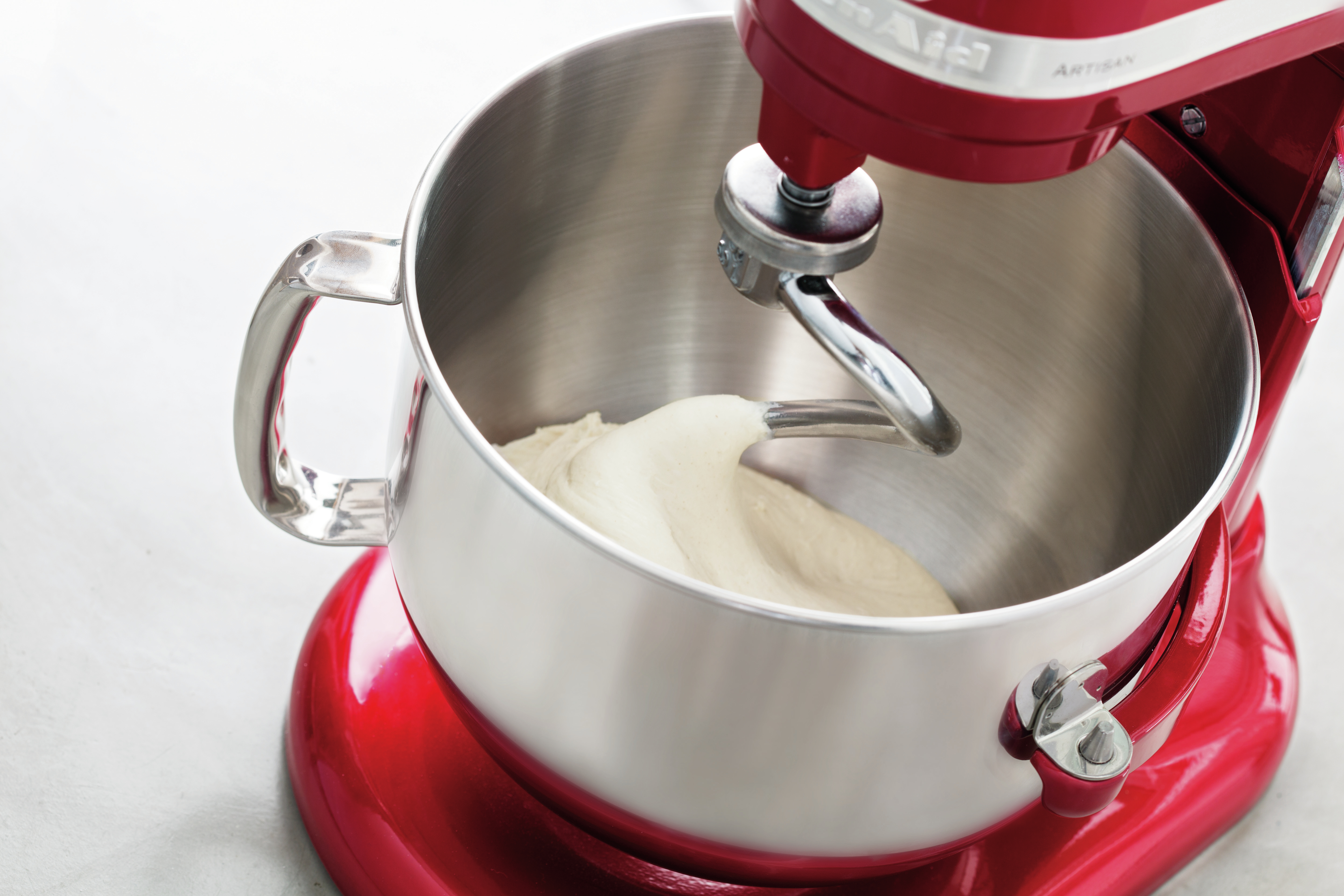 Paslanmaz çelik bir kapta hamurla kırmızı bir KitchenAid mikser. Mikserin bir hamur kancası var.